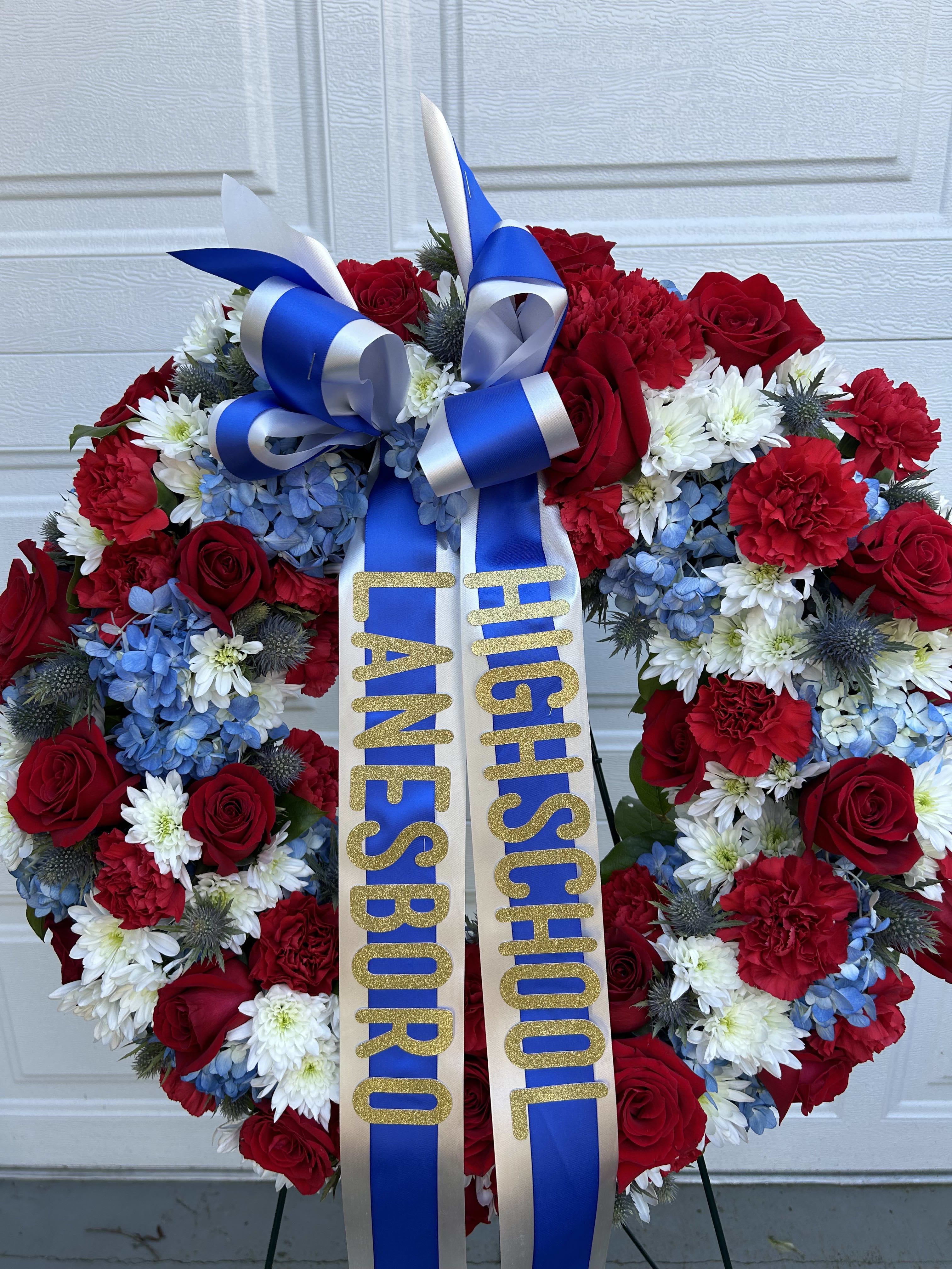 Heart-shaped floral wreath with red, white, and blue flowers and a ribbon