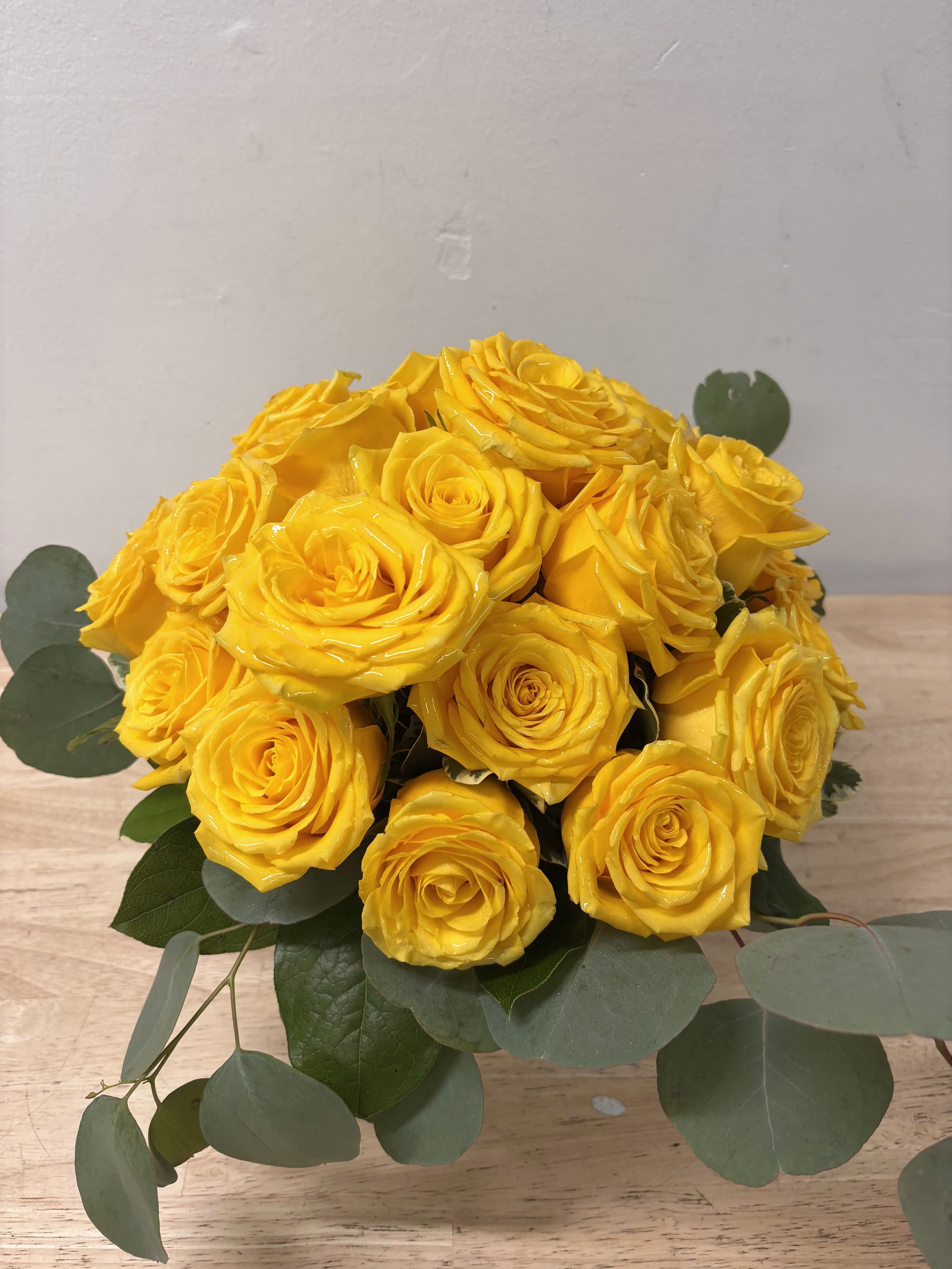 Bouquet of yellow roses with eucalyptus on a wooden surface