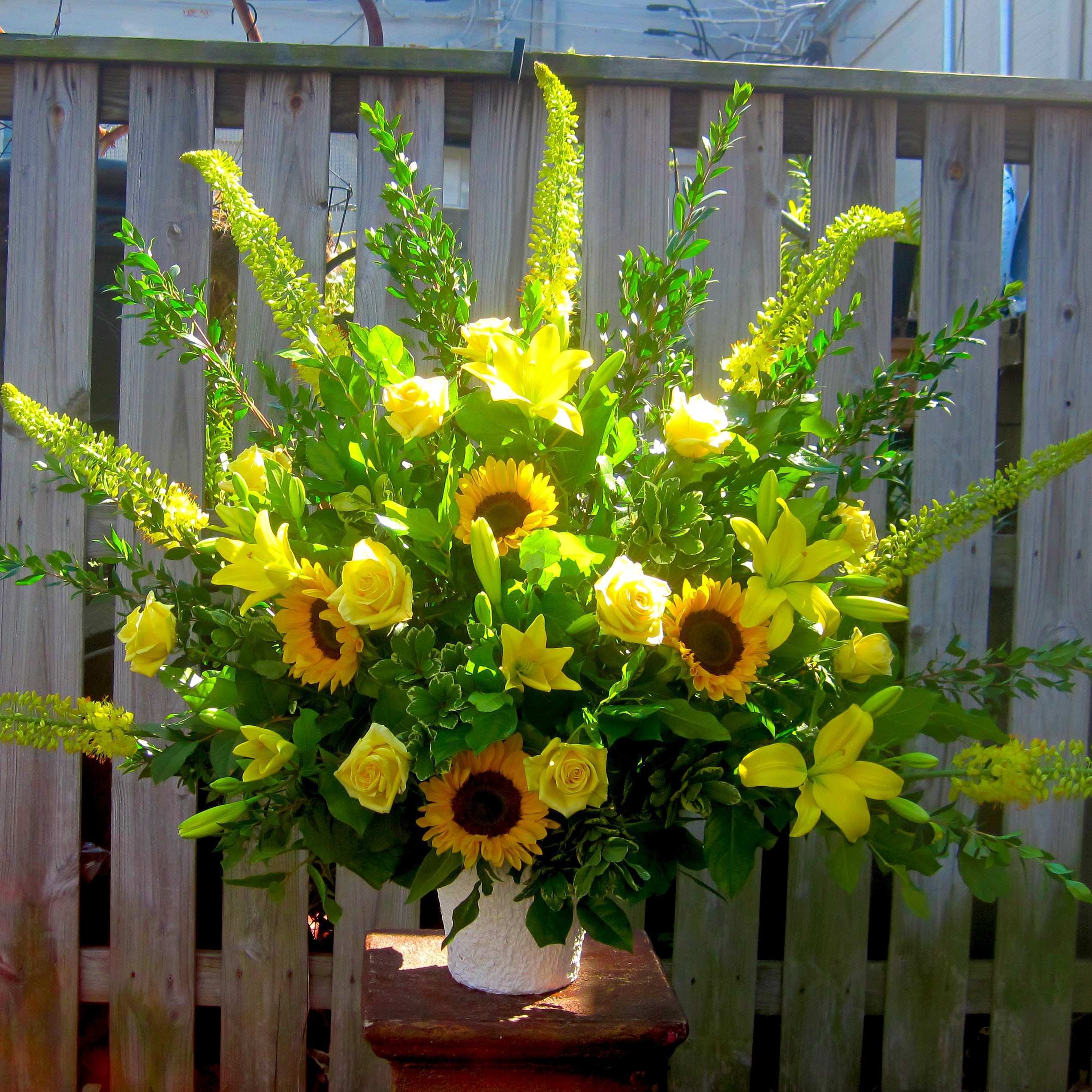 Yellow floral arrangement with sunflowers, roses, and lilies in a white vase