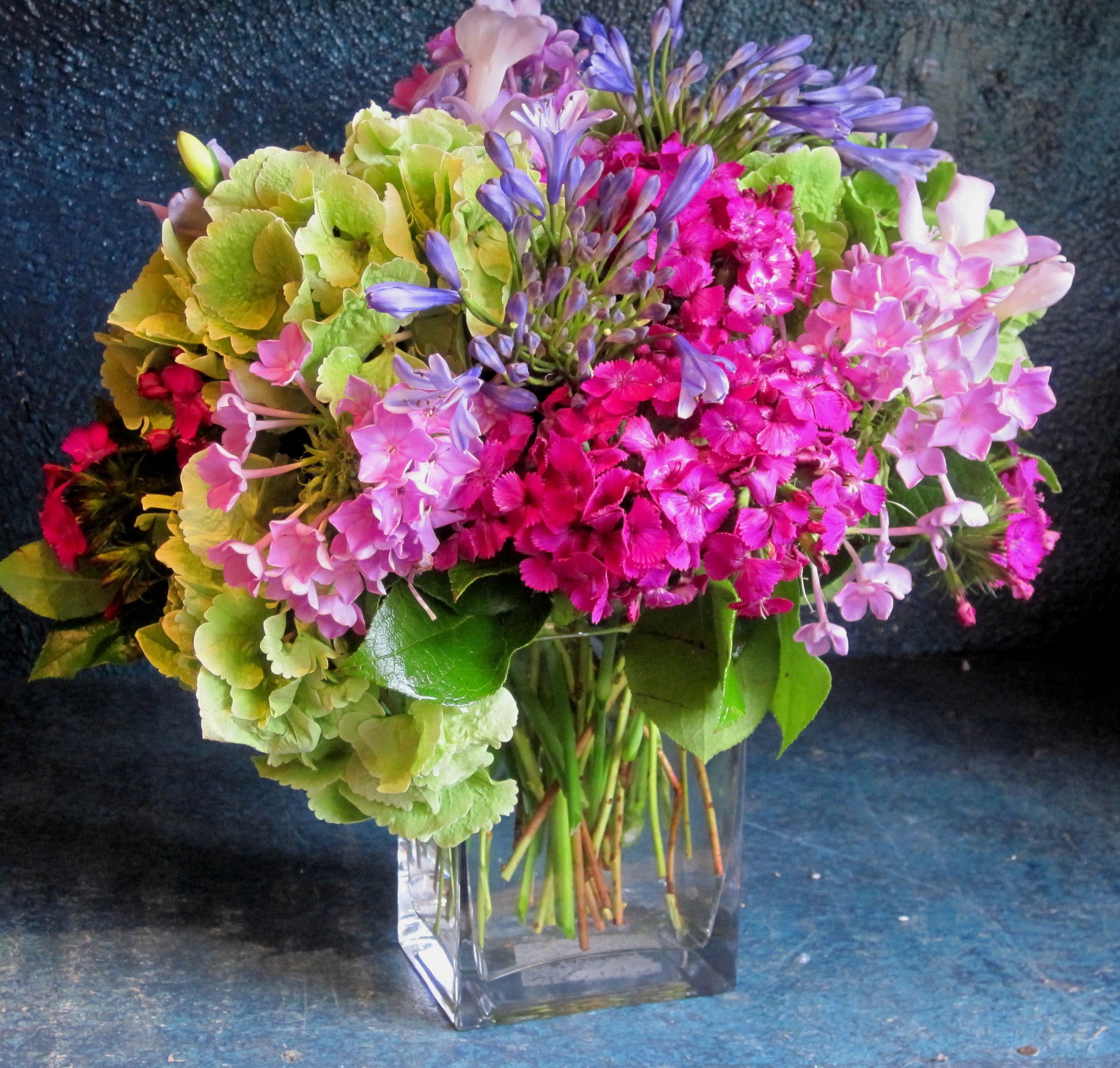 Mixed bouquet of pink blooms, green hydrangeas, and purple flowers in a clear glass cube vase