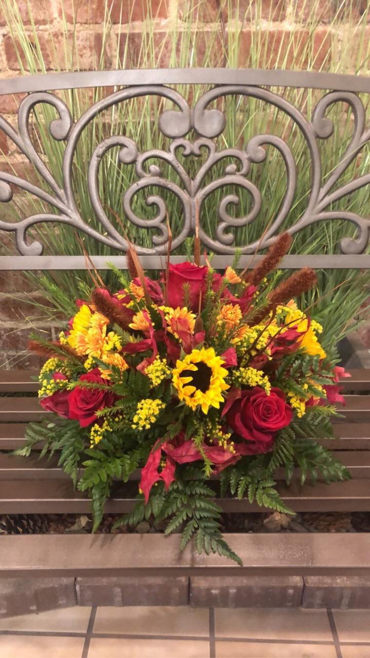 Gathered Together - Thanksgiving centerpiece filled with fresh fall blooms, in colors of bronze, yellow, burgundy, and red. Accented with preserved leaves, and wheat. 