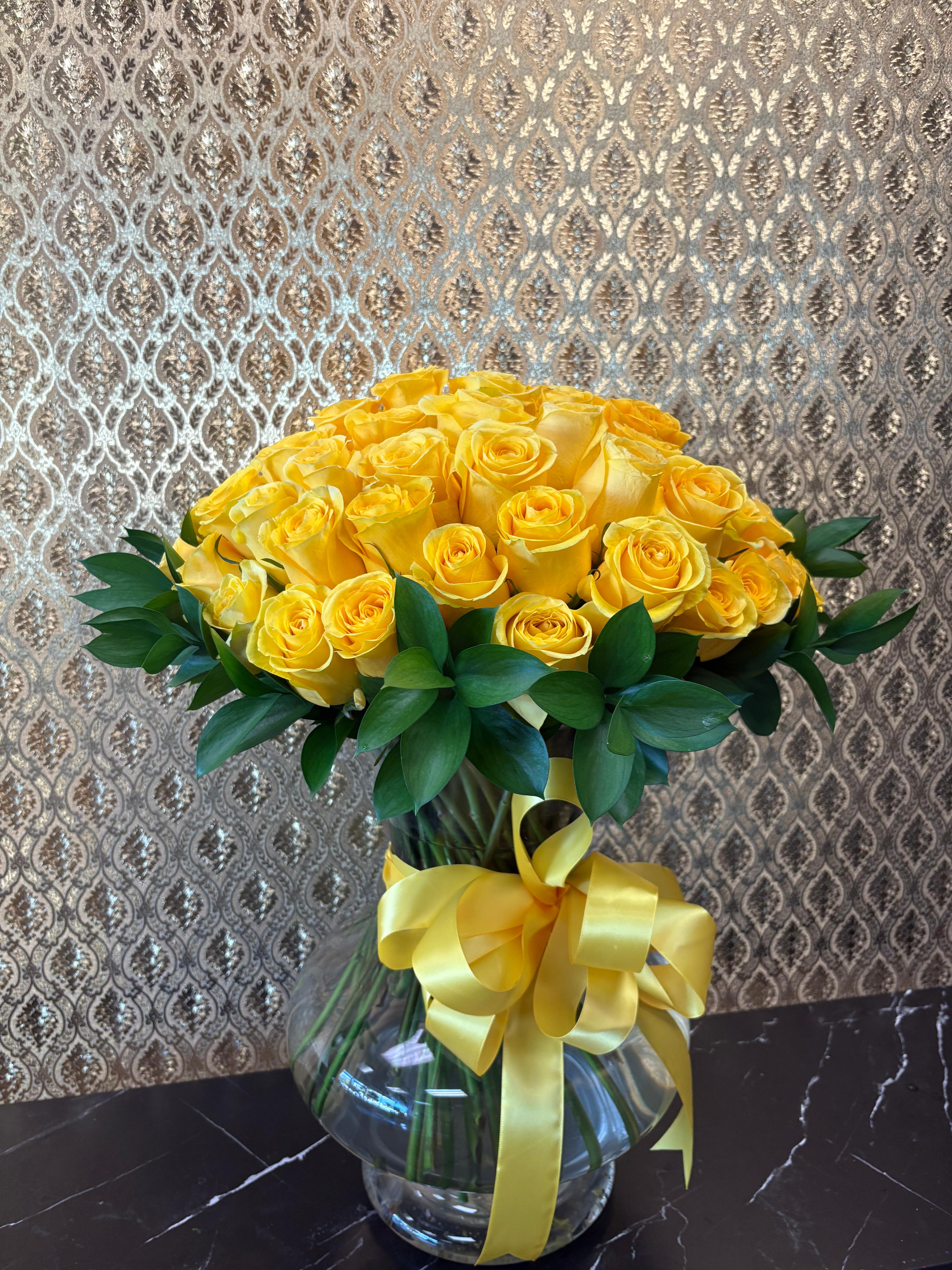 Yellow rose bouquet in a clear glass vase with a yellow ribbon