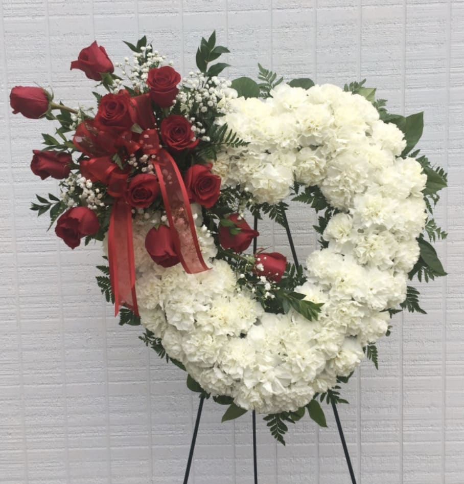 Heart-shaped floral wreath with red roses and white flowers on a stand