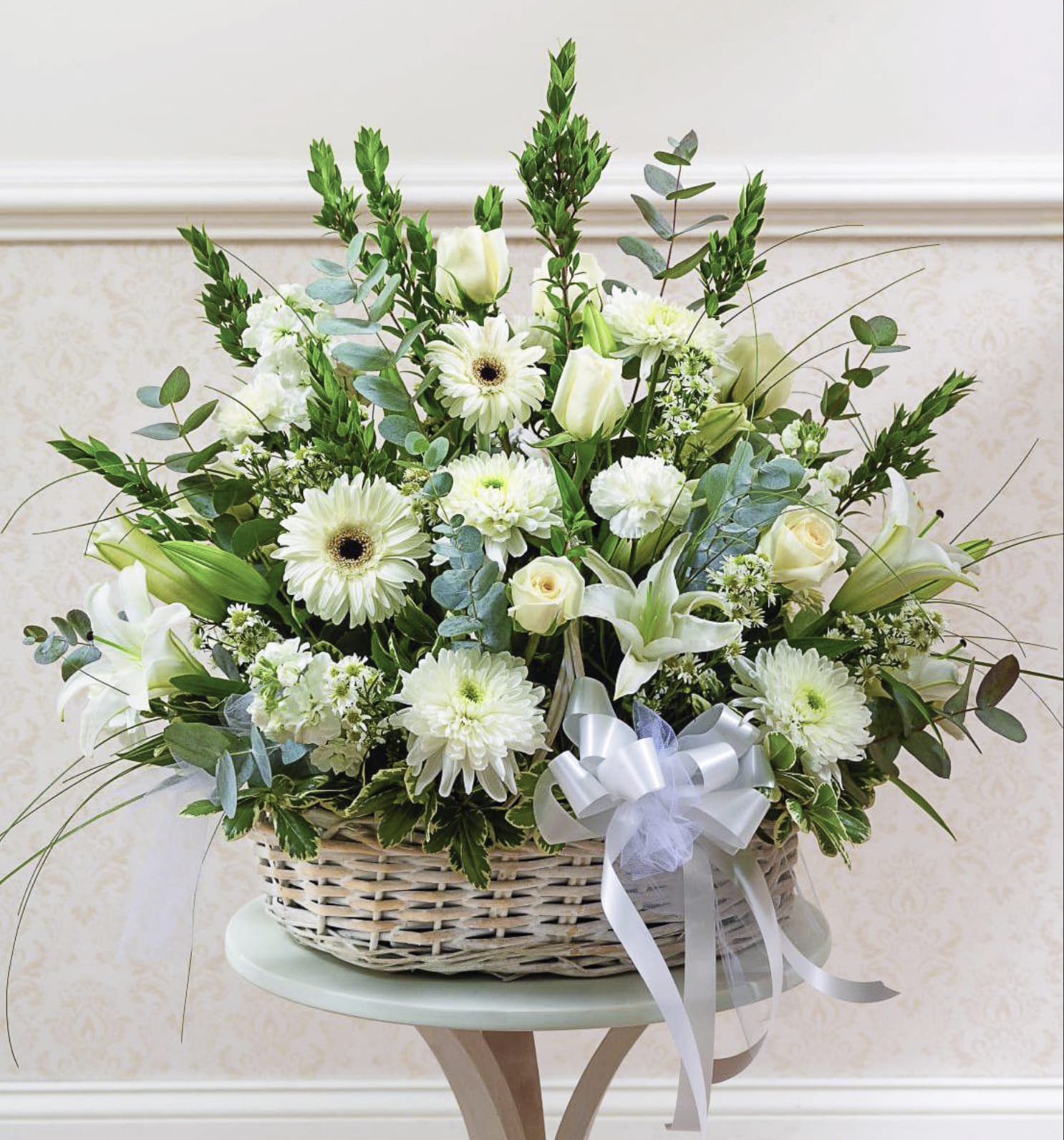 White floral arrangement in a wicker basket with a ribbon bow