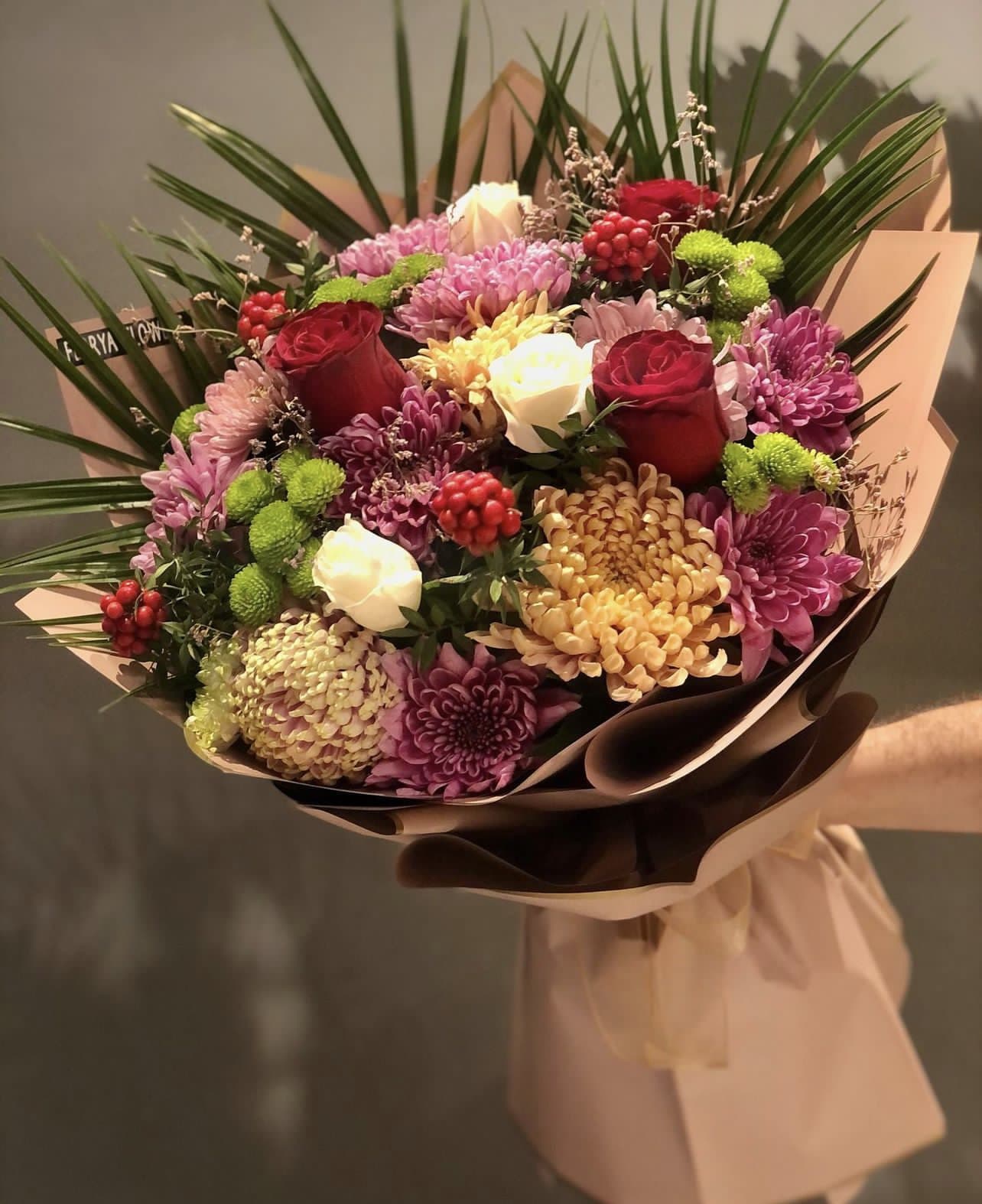 Bouquet of red roses, chrysanthemums, and white blooms wrapped in paper