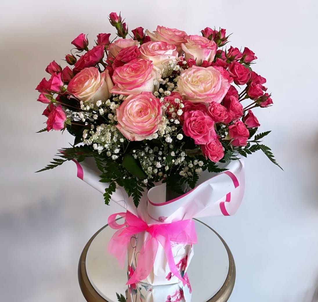 Pink and cream roses arranged in a wrapped bouquet with a pink ribbon