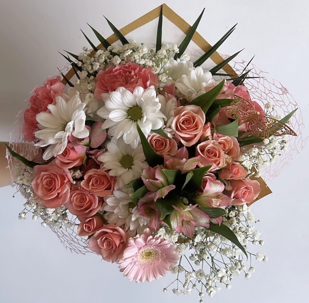 Pink roses and white daisies arranged with baby's breath in a decorative wrap