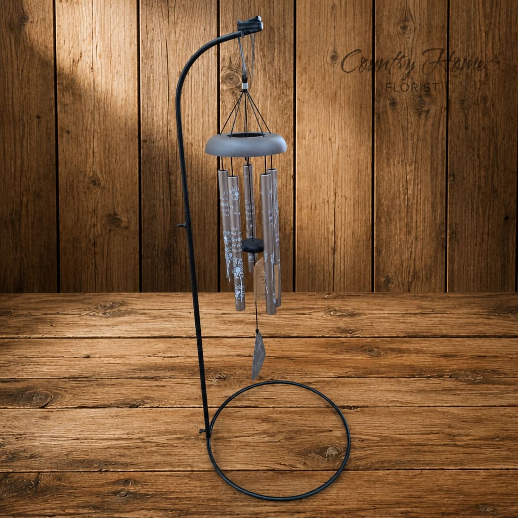 Metal wind chime hanging from a black stand on a wooden floor