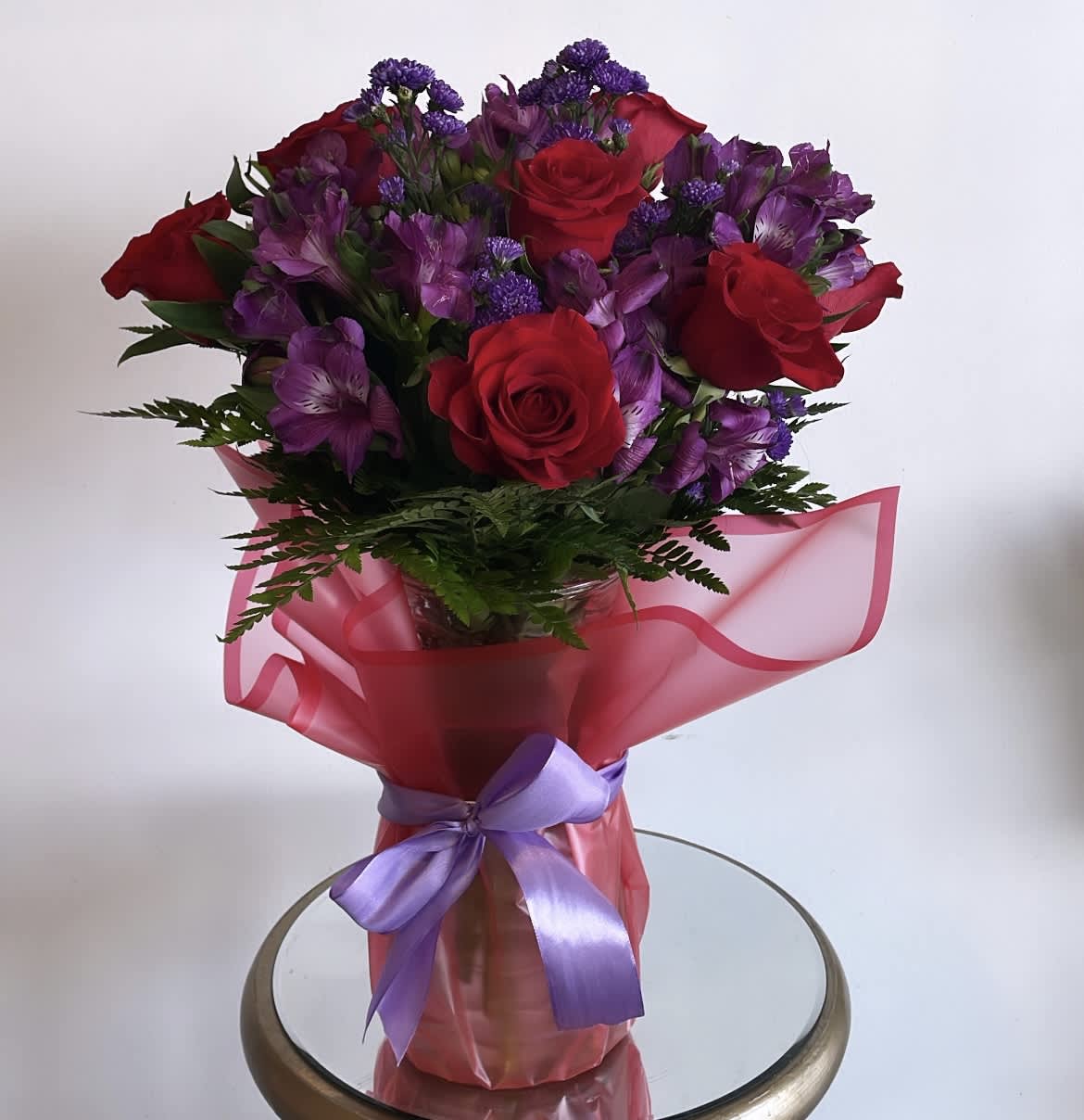 Bouquet of red roses and purple flowers wrapped in pink paper with a lavender ribbon