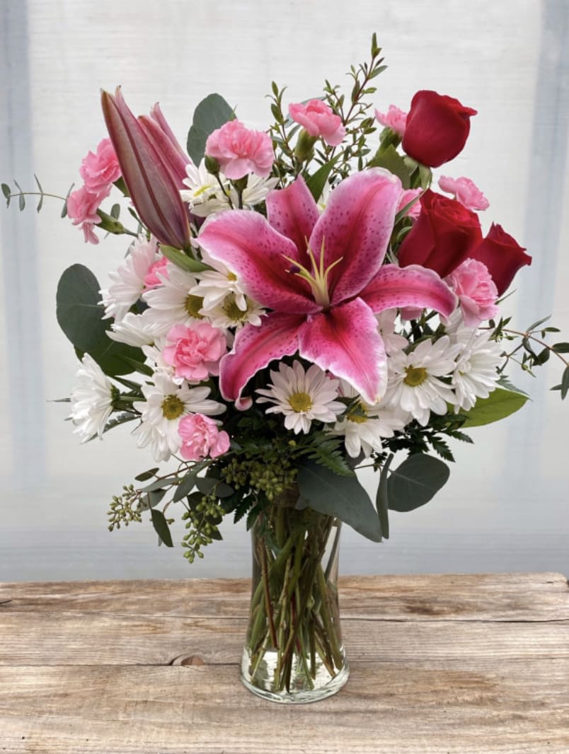 Pink lilies, roses, and daisies arranged in a clear glass vase