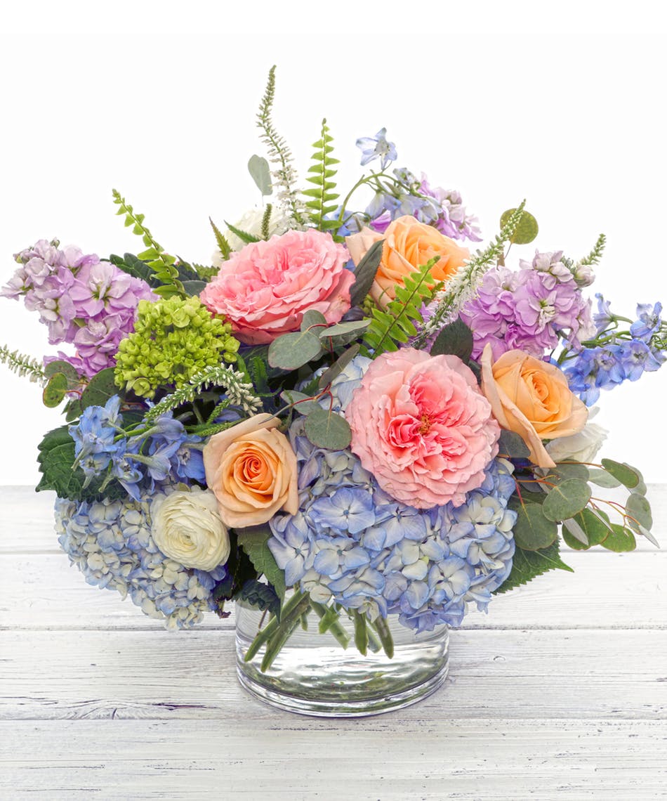 English Garden  - Spring favorites include white hydrangea, pastel garden roses, lavender scented stock and garden blue thistle nestled in silver eucalyptus and presented in one of our chic glass vases perfect for any table, credenza or desk.  Hand-delivered with your sentiment and guaranteed to make the perfect impression.   PLEASE NOTE: Florist reserves the right to make modifications to the design based on seasonality and accessibility of blooms and vases. Any modifications made will honor the palette, intent, and feeling of the pictured design. Contact floral designer directly with any specifications or concerns.