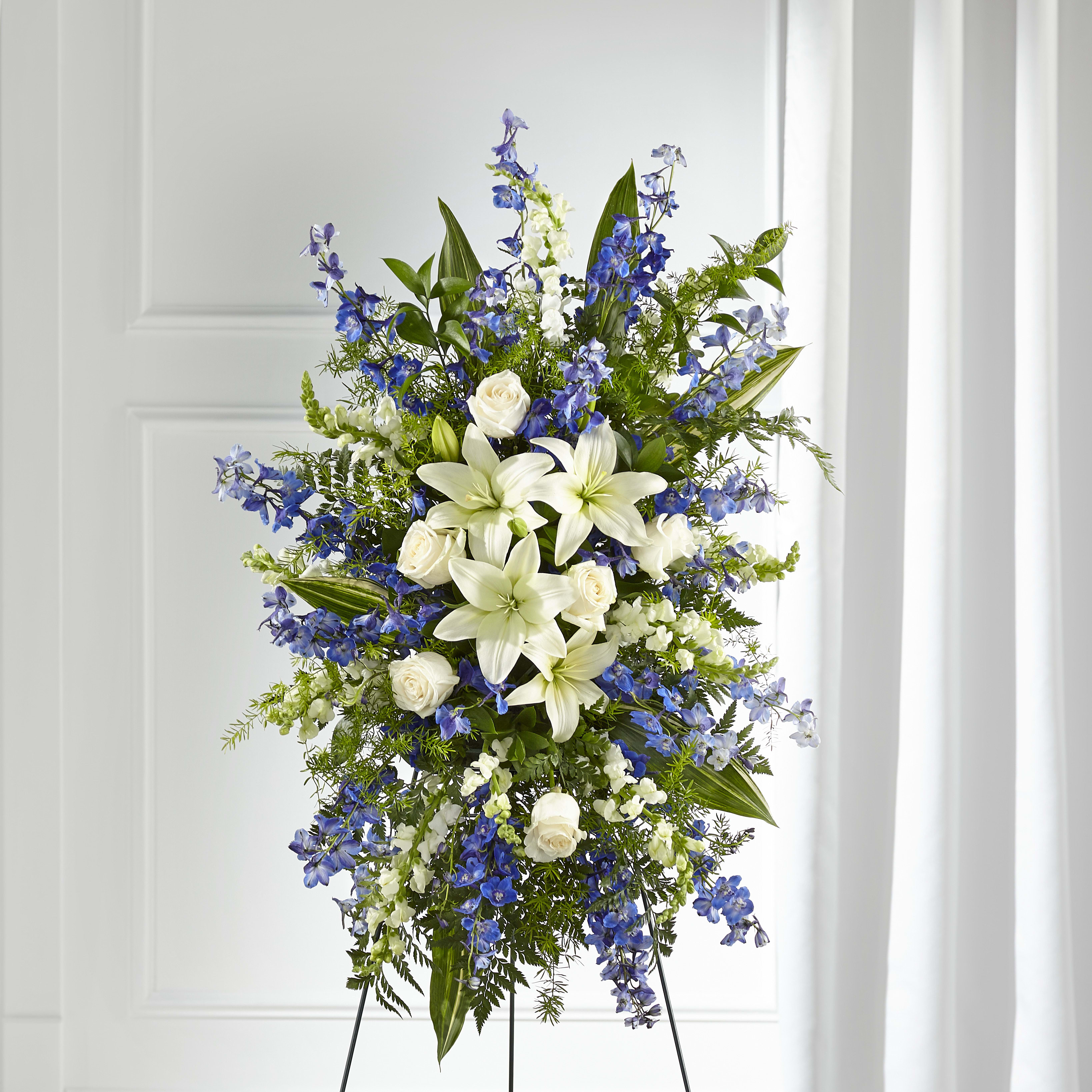 Standing spray of white lilies and roses with blue delphinium on a metal easel