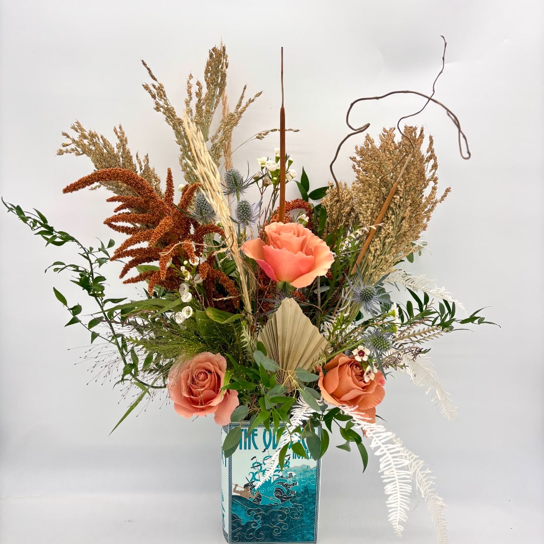 Tall arrangement with peach roses and dried grasses in a decorative container