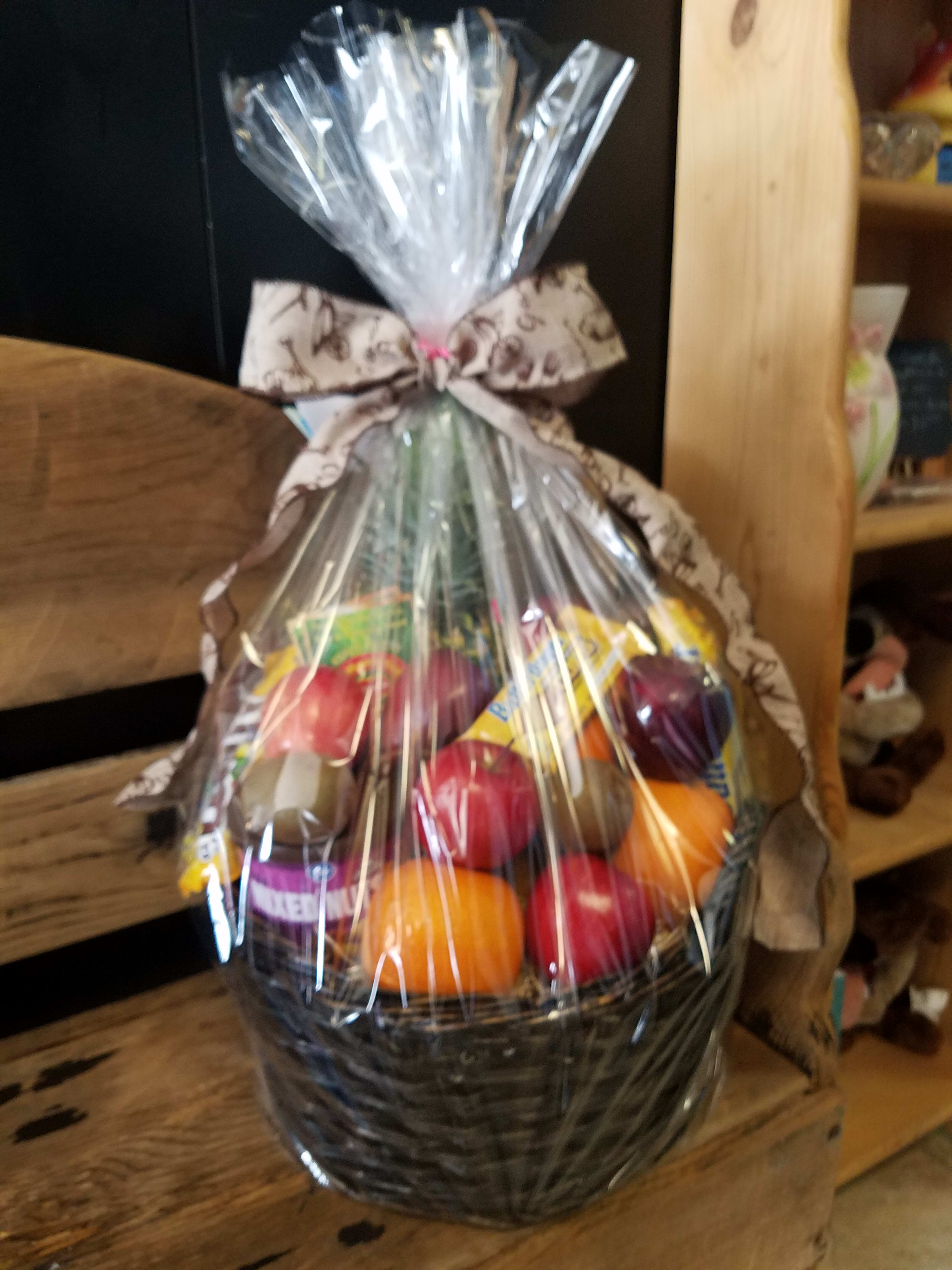 Cellophane-wrapped fruit and snack gift basket tied with a patterned bow.