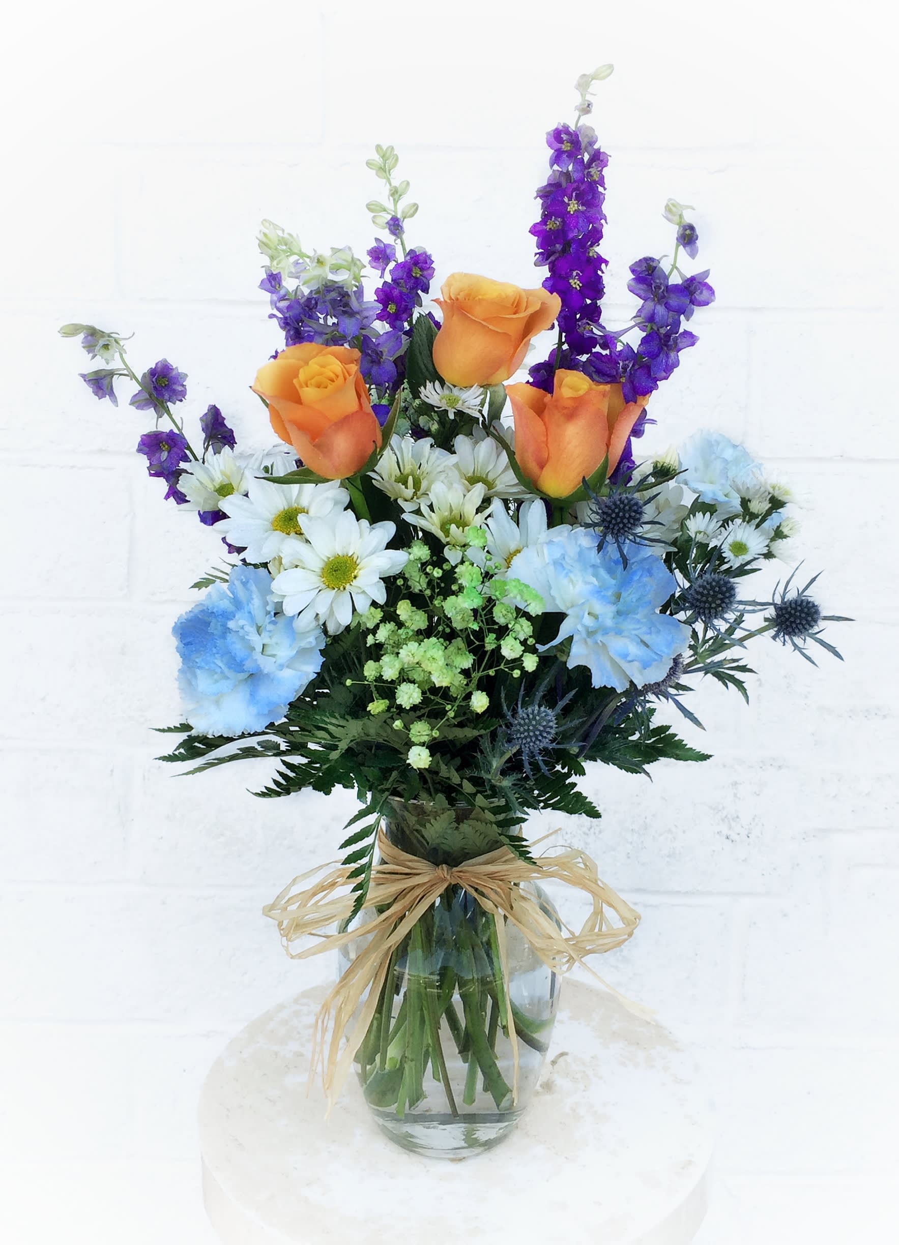 Bouquet of orange roses, blue carnations, and purple flowers in a glass vase