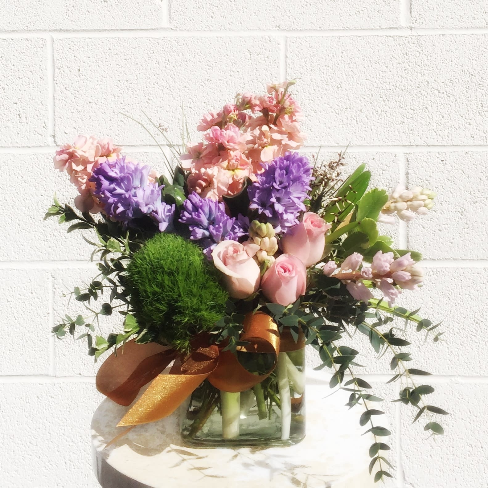 Pink and purple flower arrangement in a glass vase with a ribbon