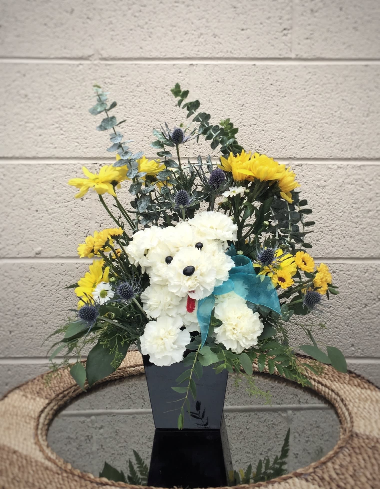 White flower arrangement shaped like a teddy bear with yellow blooms and a blue ribbon