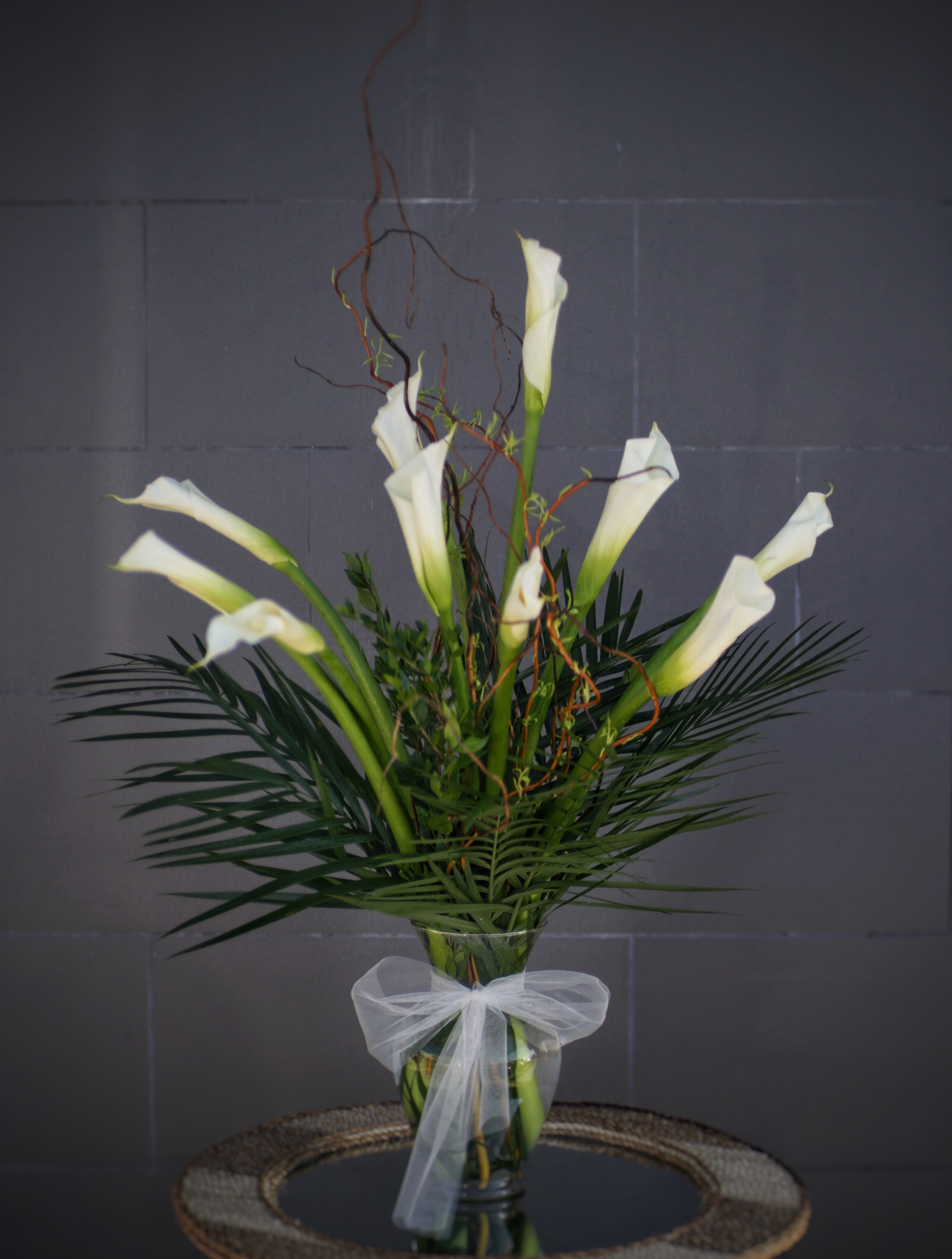 Tall arrangement of white calla lilies in a glass vase with a white bow