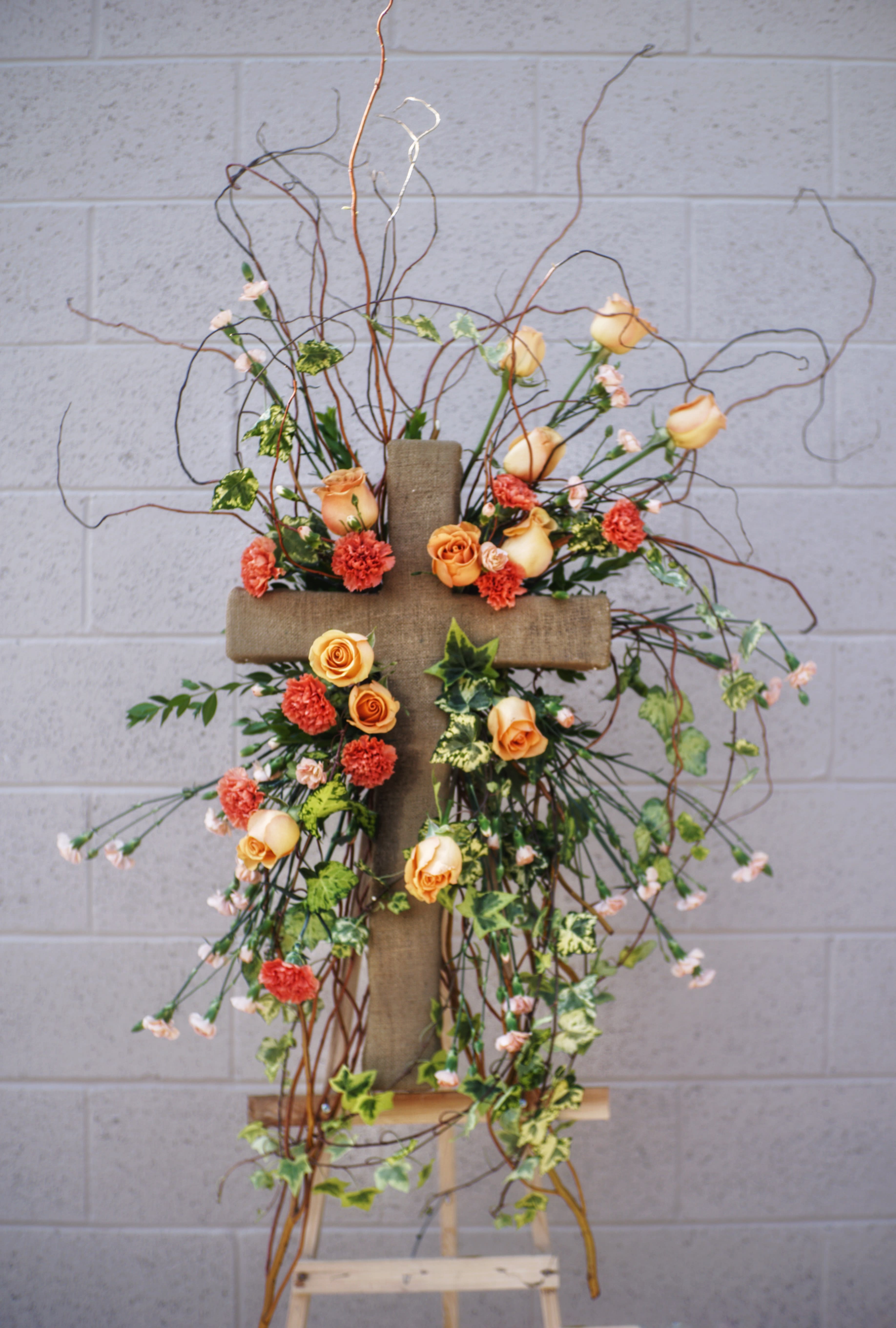 Floral cross arrangement with peach roses and orange carnations