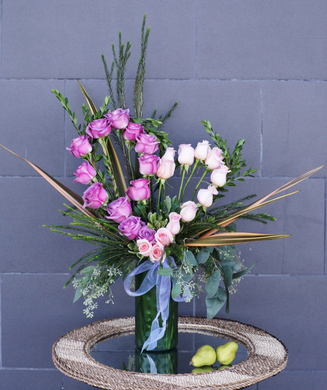 Pink and white roses in a tall green vase with ribbon