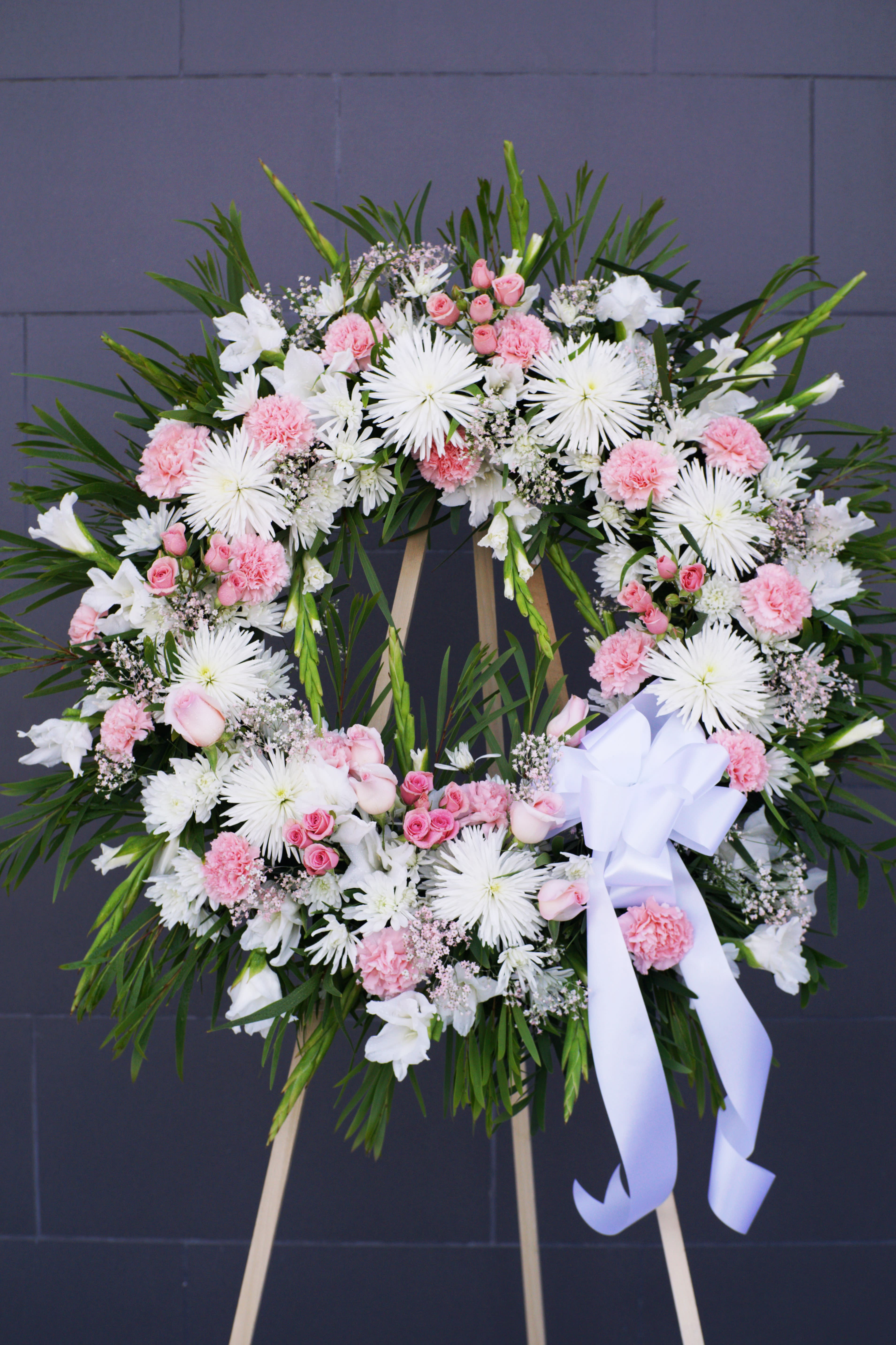 Pink and white floral wreath on a standing easel with a white ribbon
