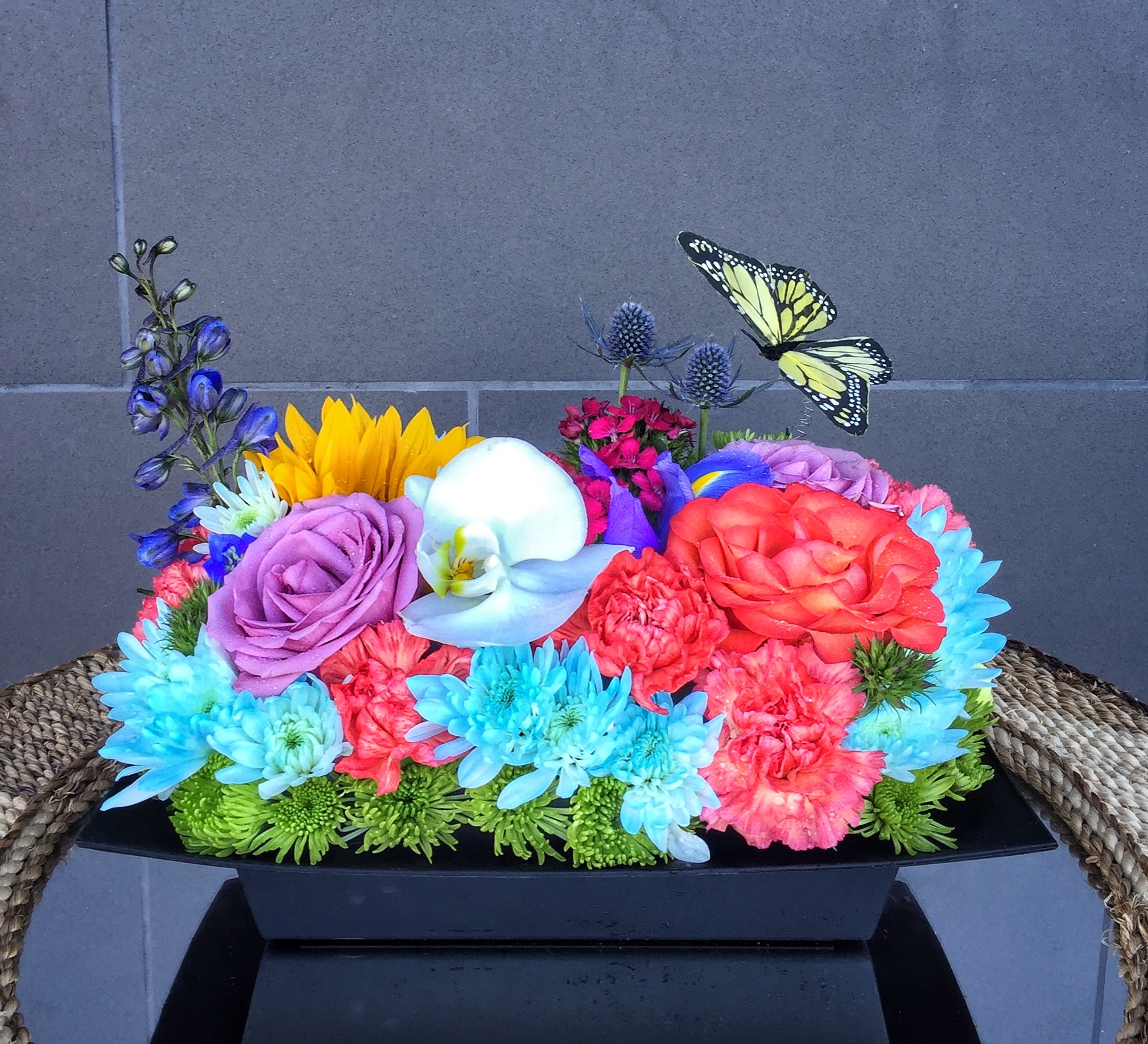 Colorful mixed flower arrangement in a black rectangular container with butterfly picks