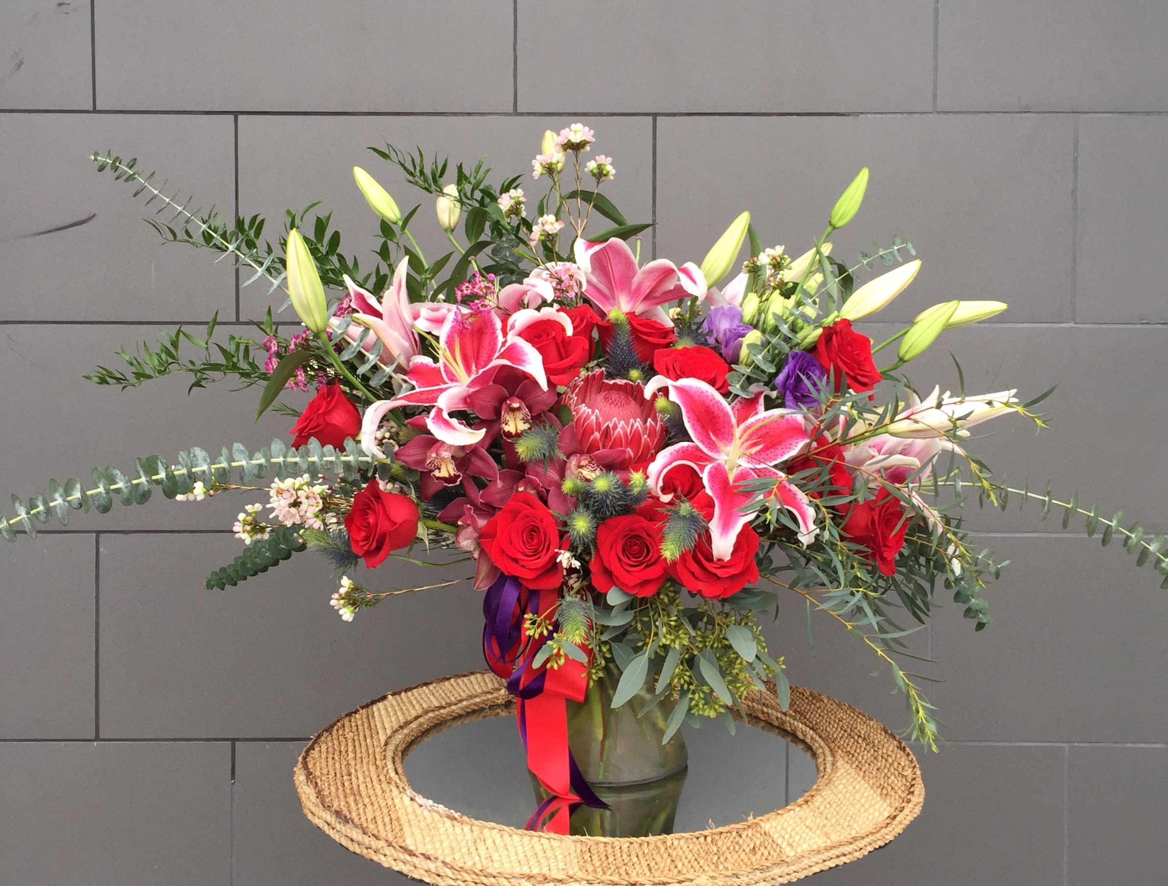 Large mixed bouquet of red roses, pink lilies, and orchids in a glass vase