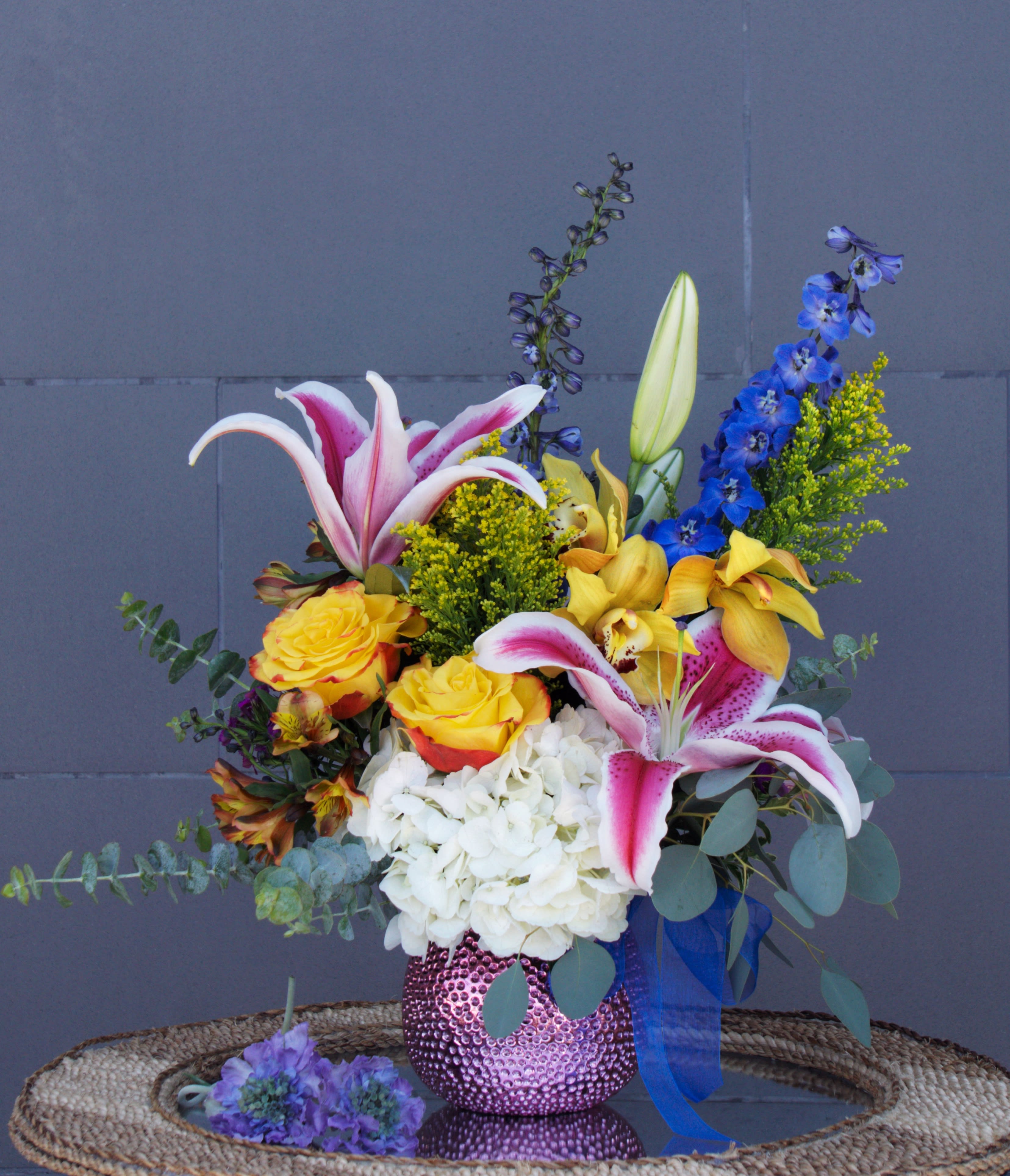 Mixed bouquet with lilies, roses, hydrangea, and blue delphinium in a pink vase