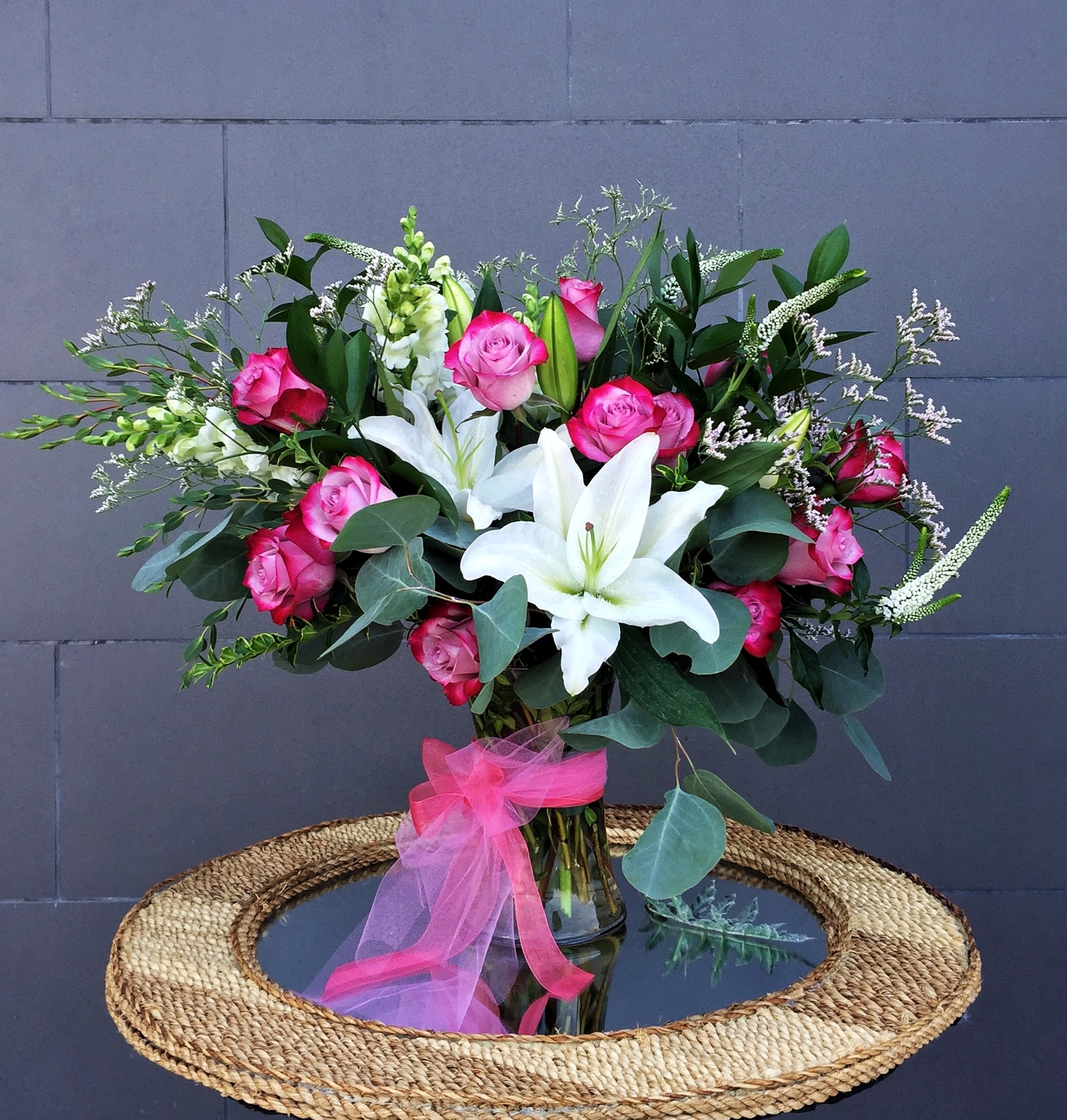 Pink roses and white lilies in a glass vase with a pink ribbon