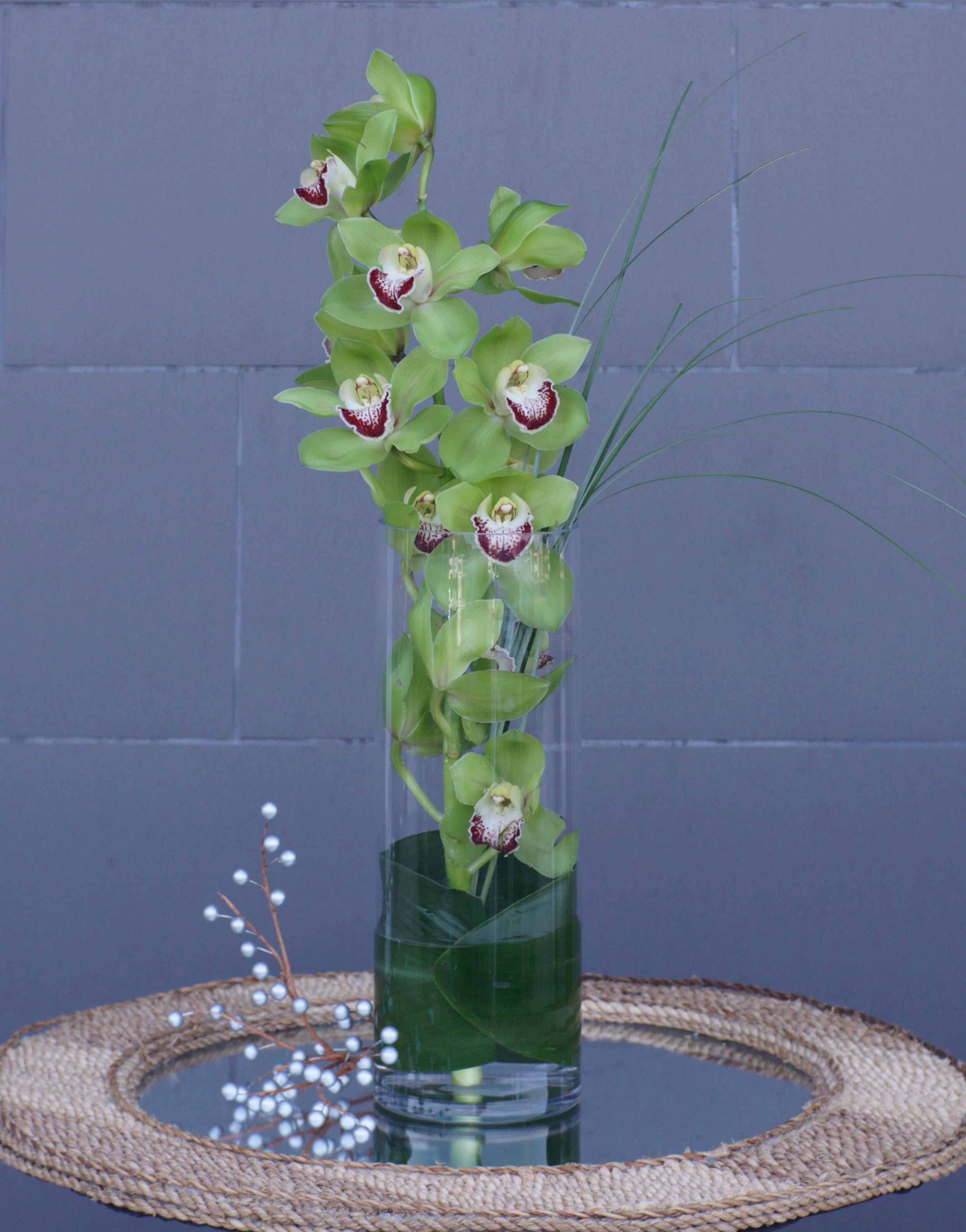 Green orchids arranged in a tall glass vase with decorative berries