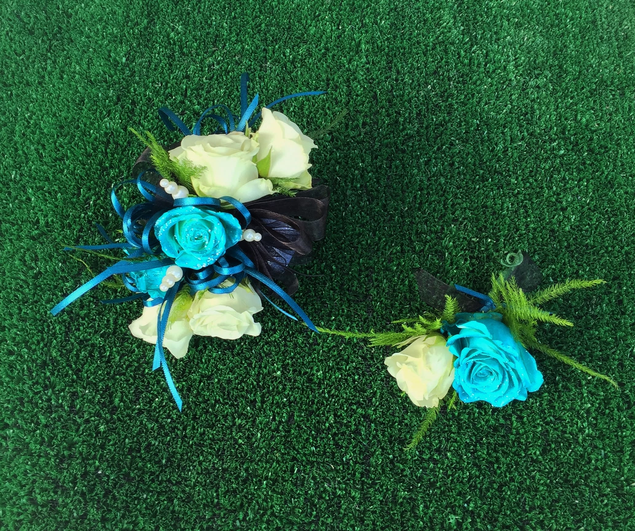 Two small rose corsages with blue ribbon accents on green turf