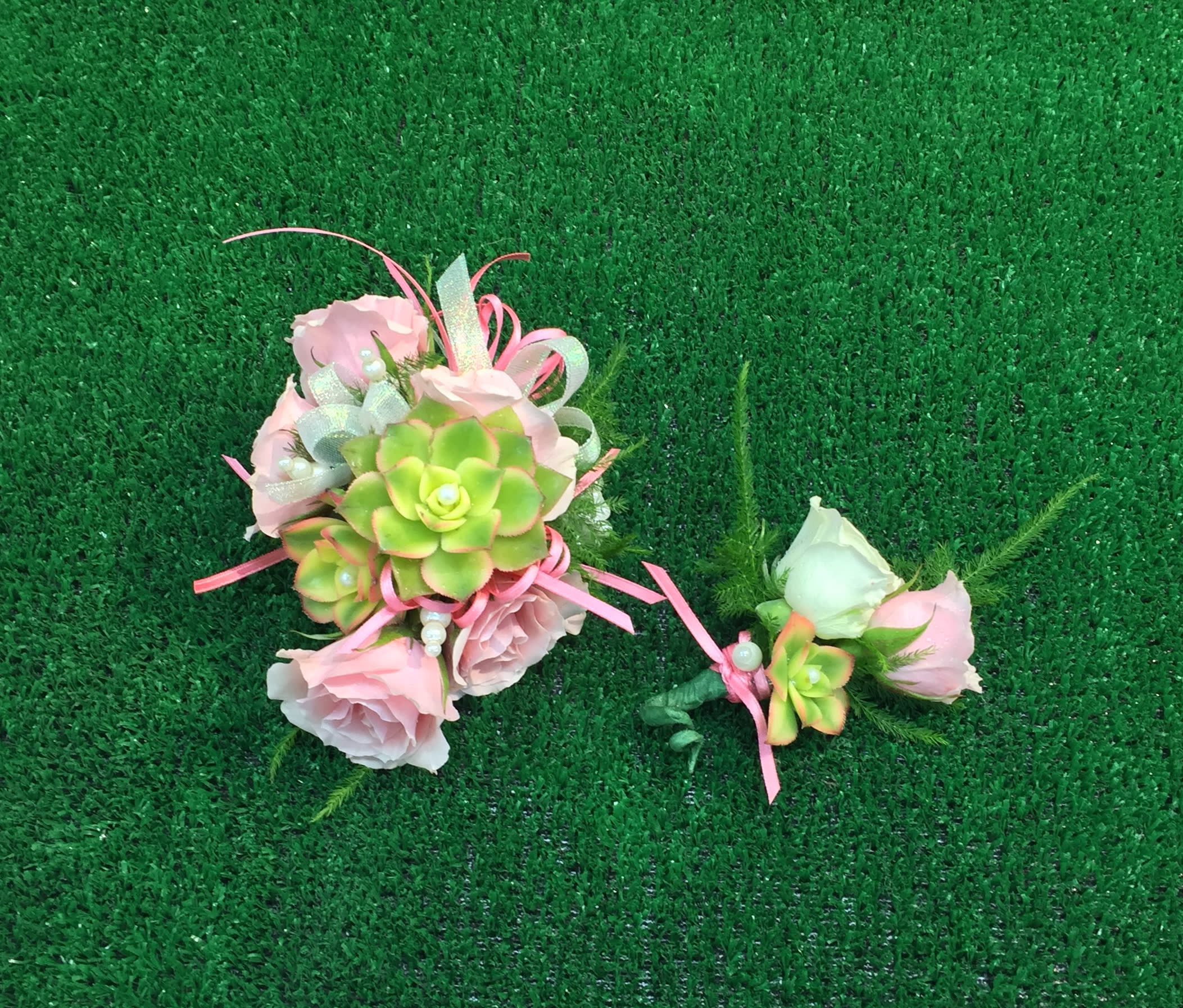 Pink floral corsage and boutonniere with succulents on green turf