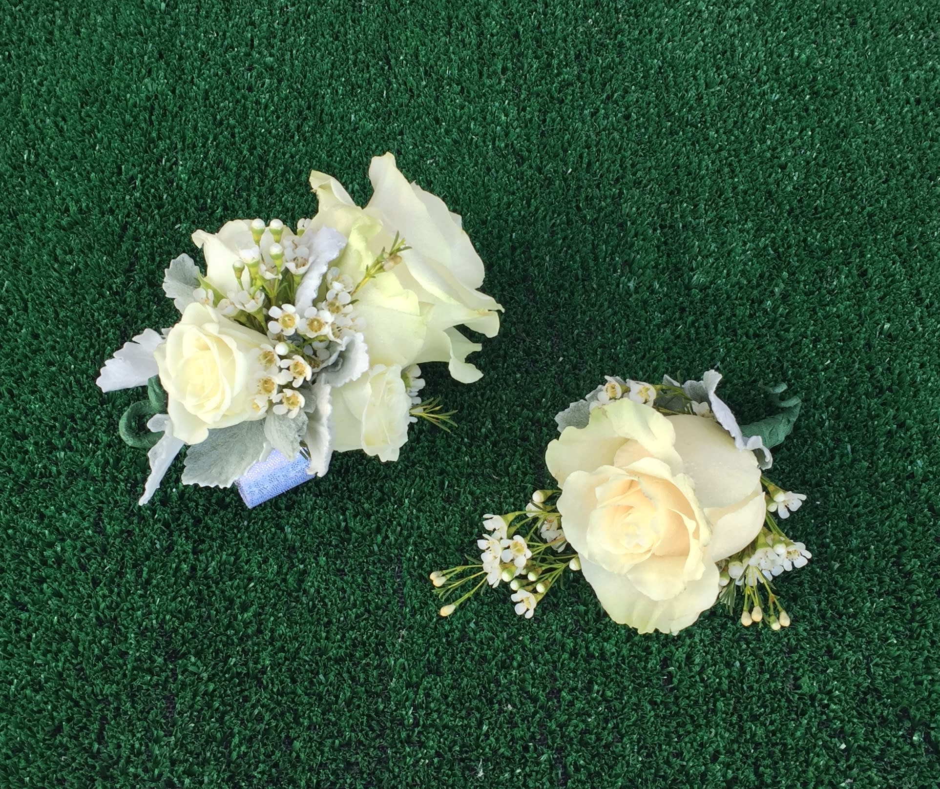 Two ivory rose corsages with small white flowers on green turf