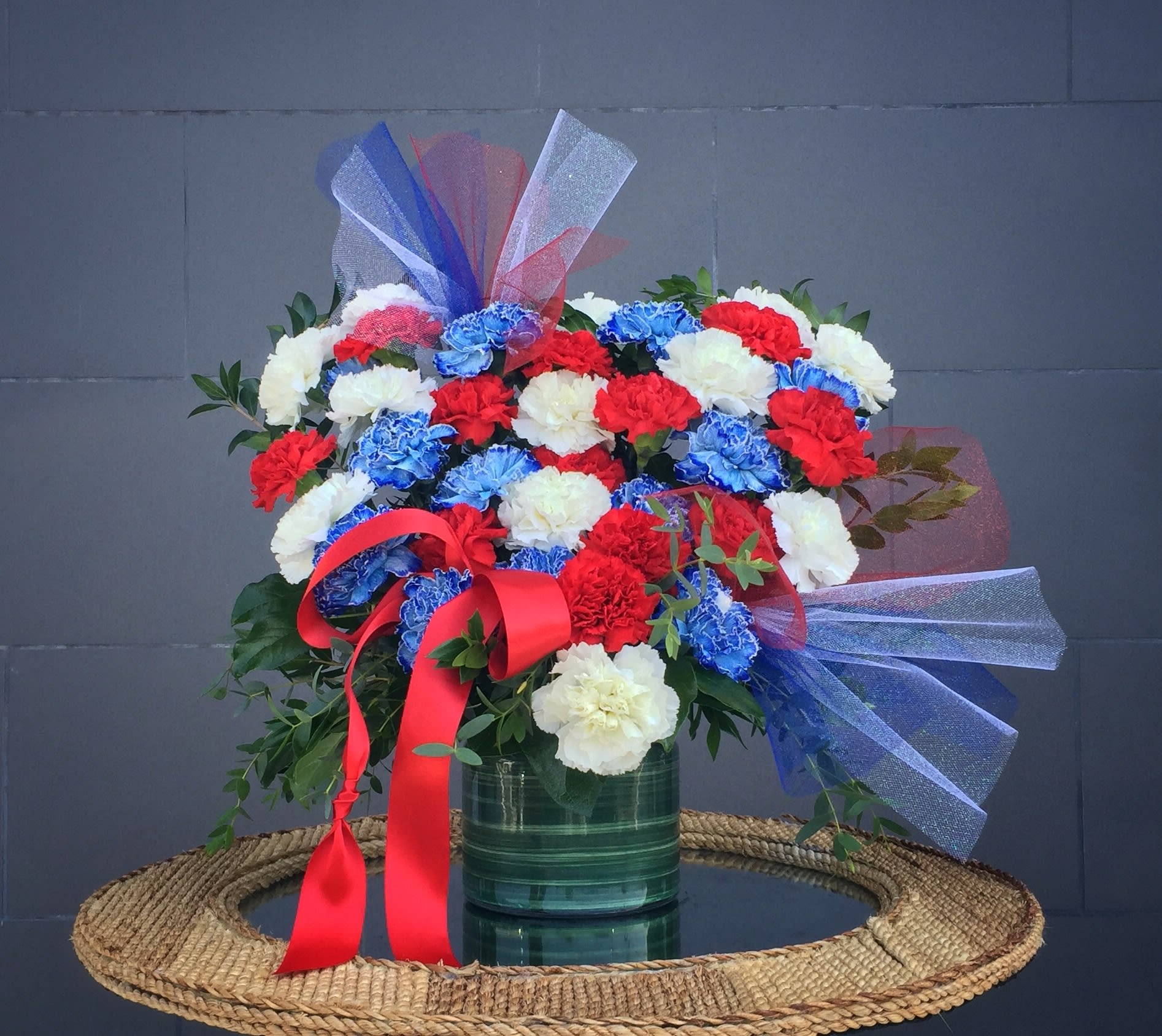 Bouquet of red, white, and blue carnations in a green vase with ribbon bows
