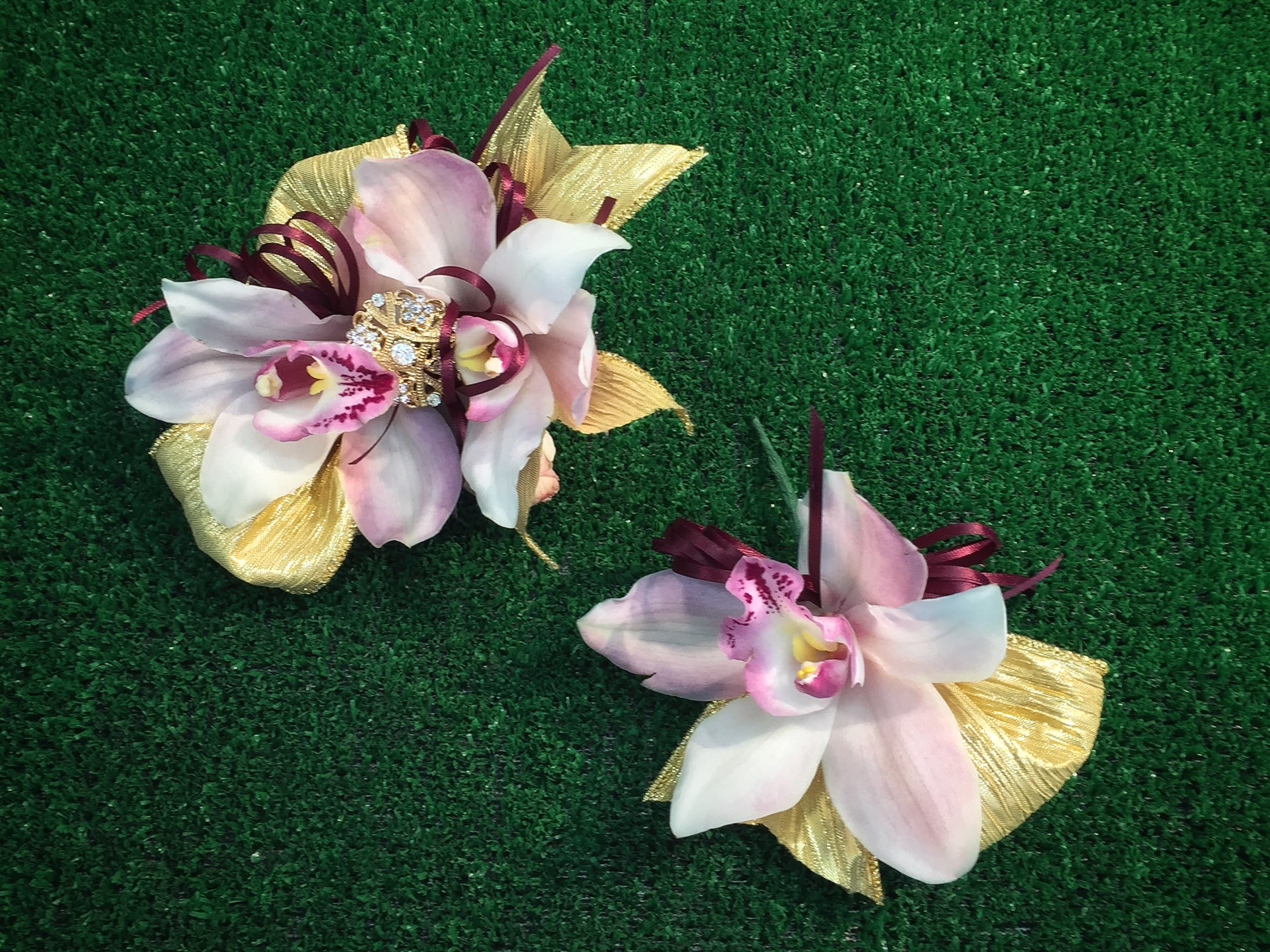 Two orchid corsages with gold ribbon accents on green turf