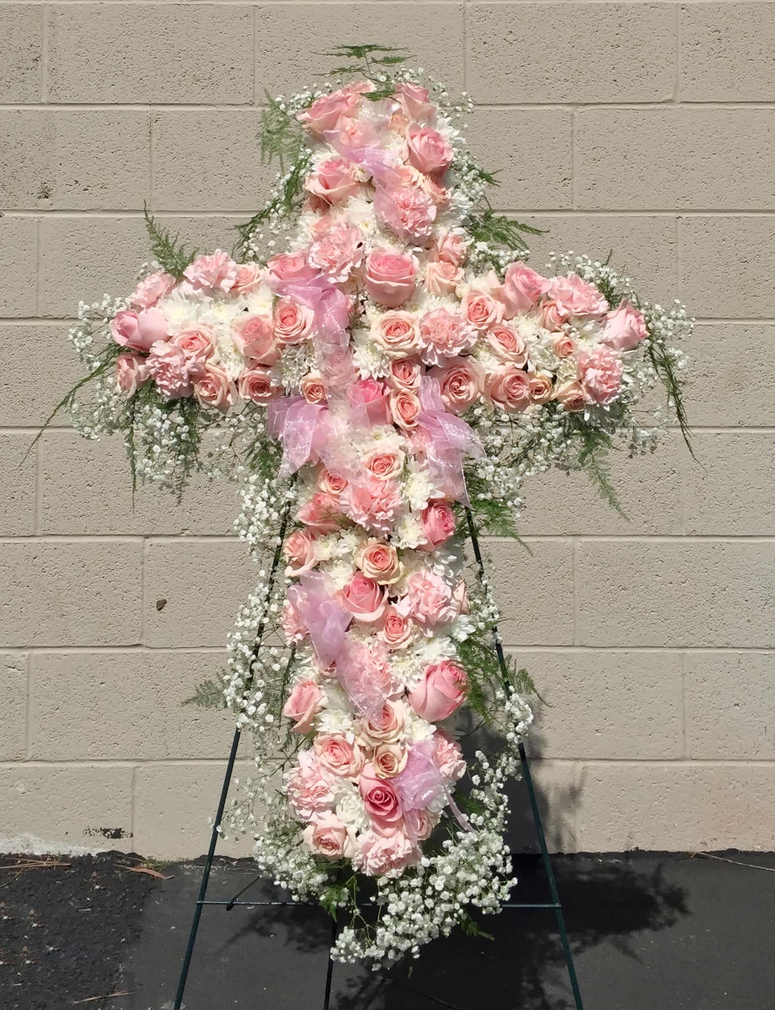 Pink floral cross on a stand with ribbon and white filler flowers