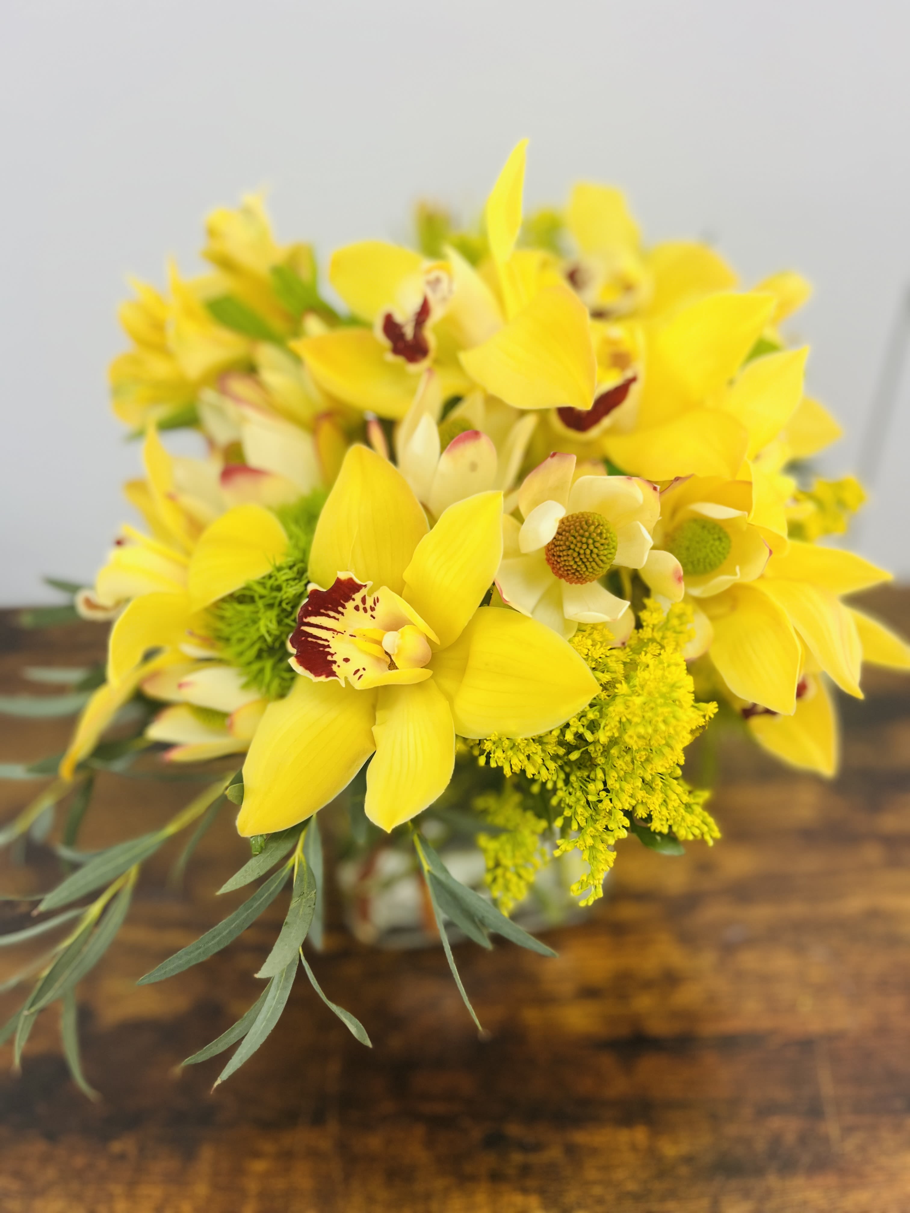 Yellow orchid bouquet with green filler in a glass vase
