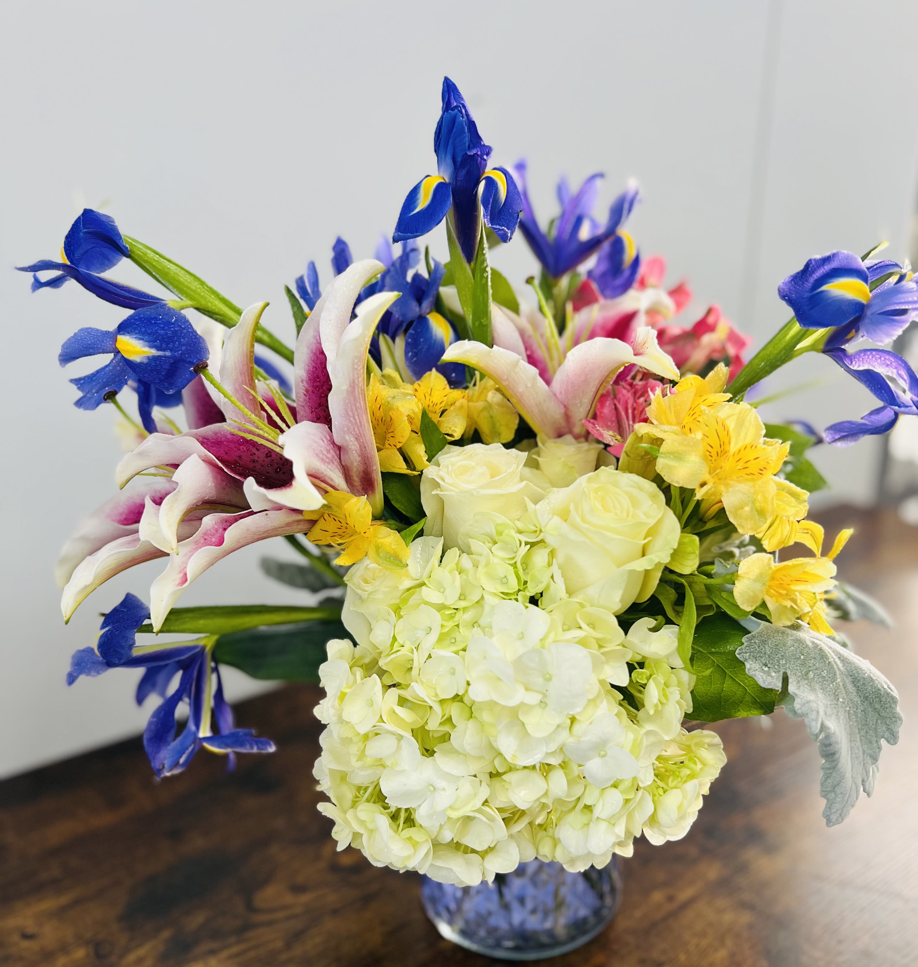 Bouquet of blue irises, white lilies, and pale hydrangeas in a glass vase
