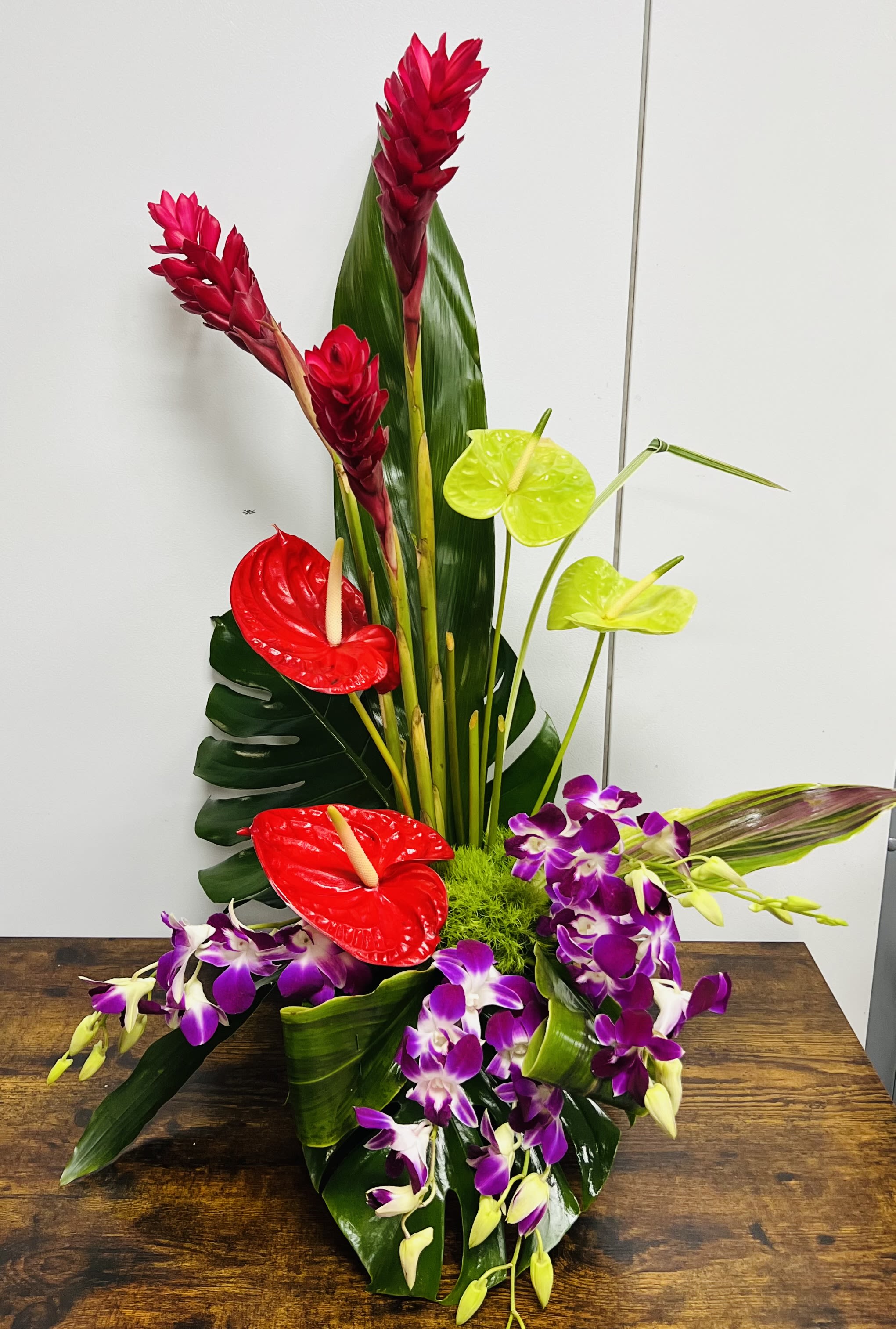 Tropical arrangement with red anthuriums, purple orchids, and tall red ginger flowers