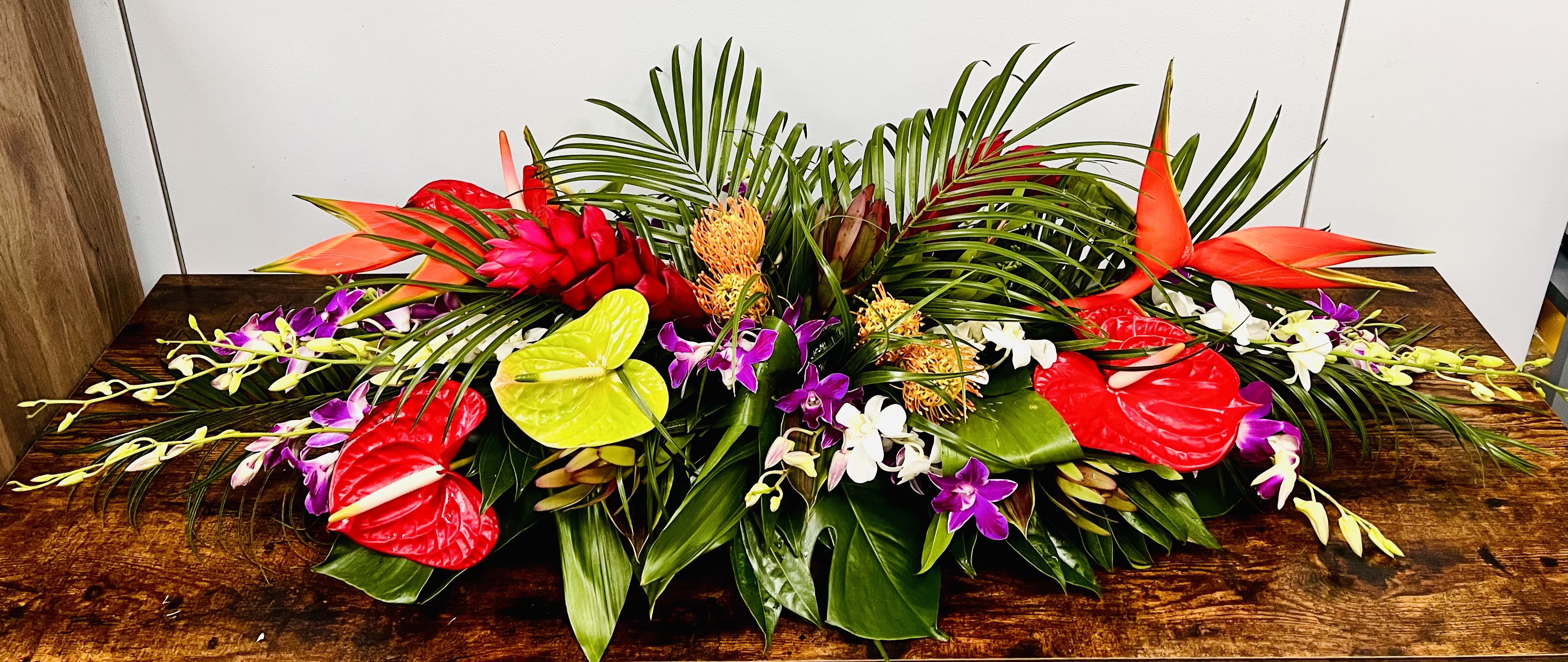 Tropical floral arrangement with red anthuriums, orchids, and palm fronds