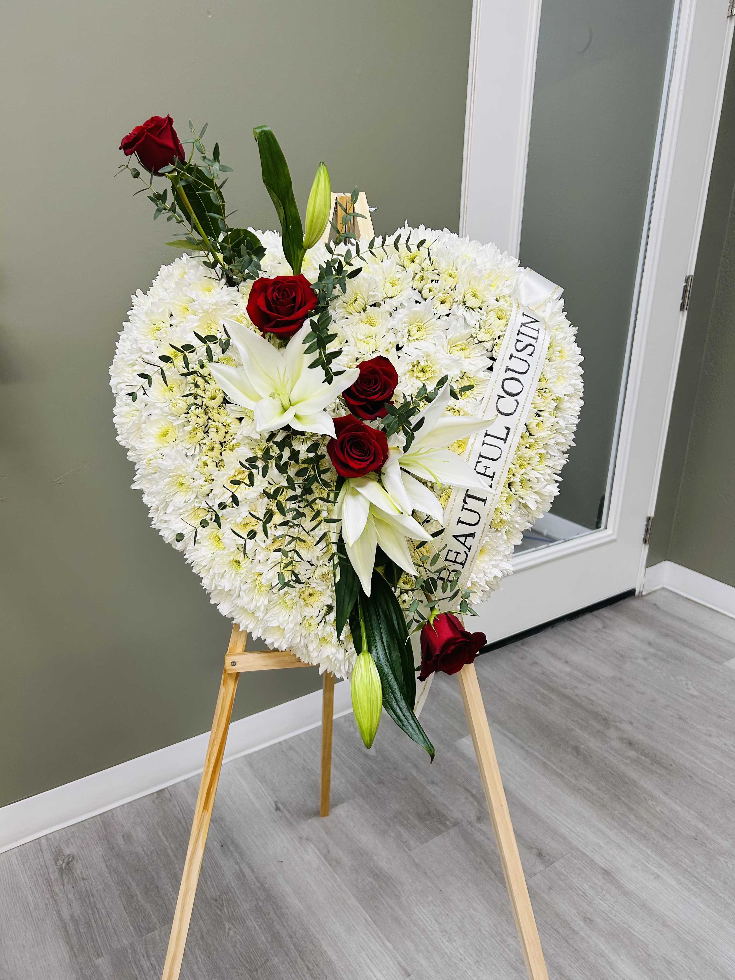 Heart-shaped white floral wreath with red roses and lilies on an easel