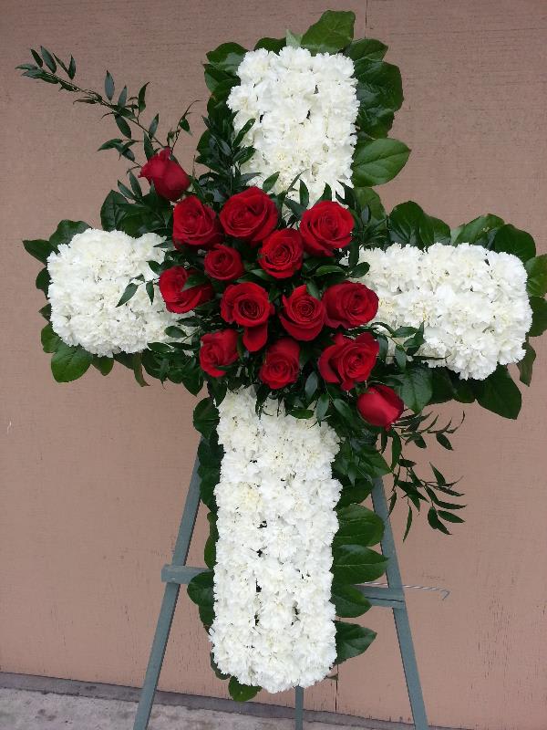 Cross-shaped floral tribute with red roses and white flowers on an easel