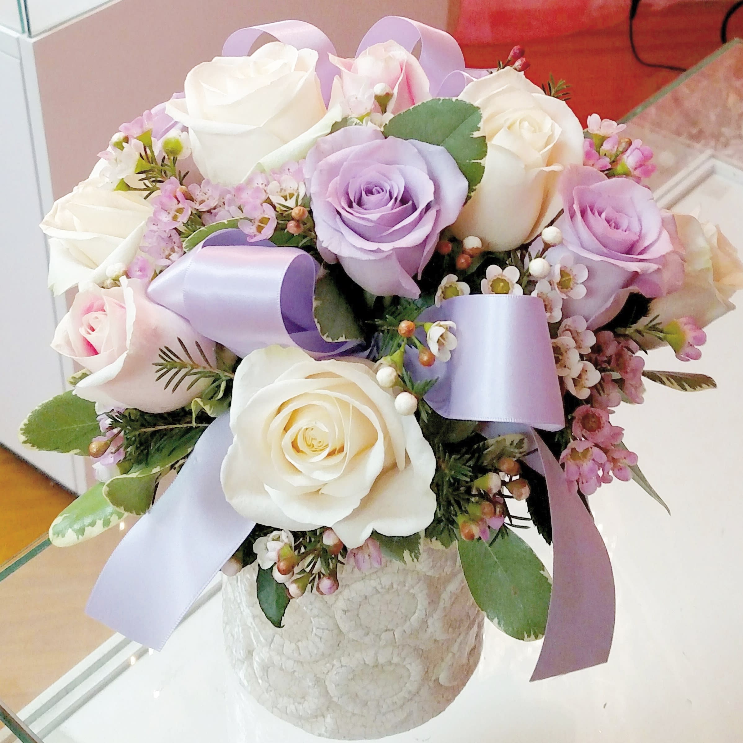 Bouquet of white and lavender roses with lilac ribbon in a textured vase