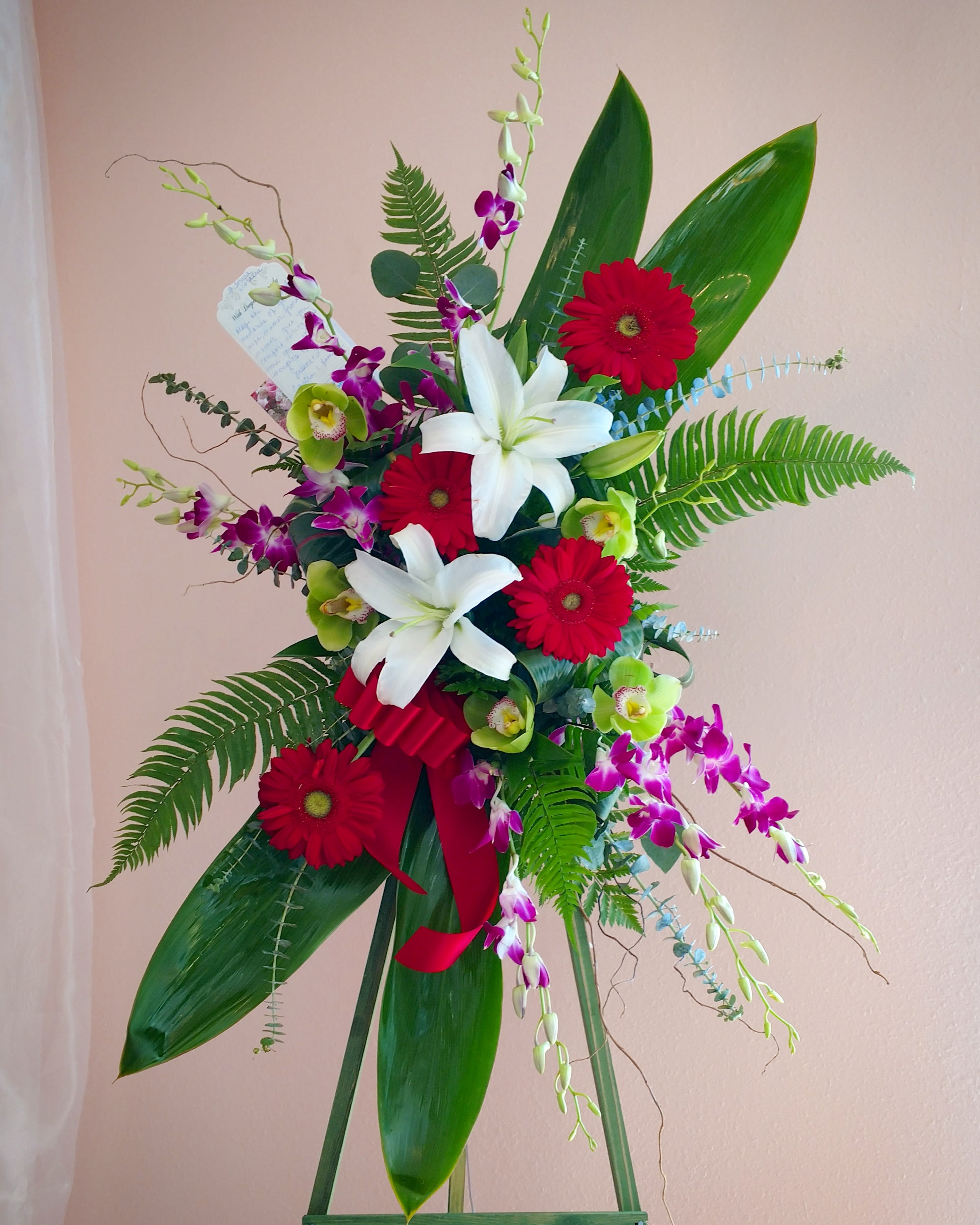 Standing floral spray with red gerberas, white lilies, and purple orchids
