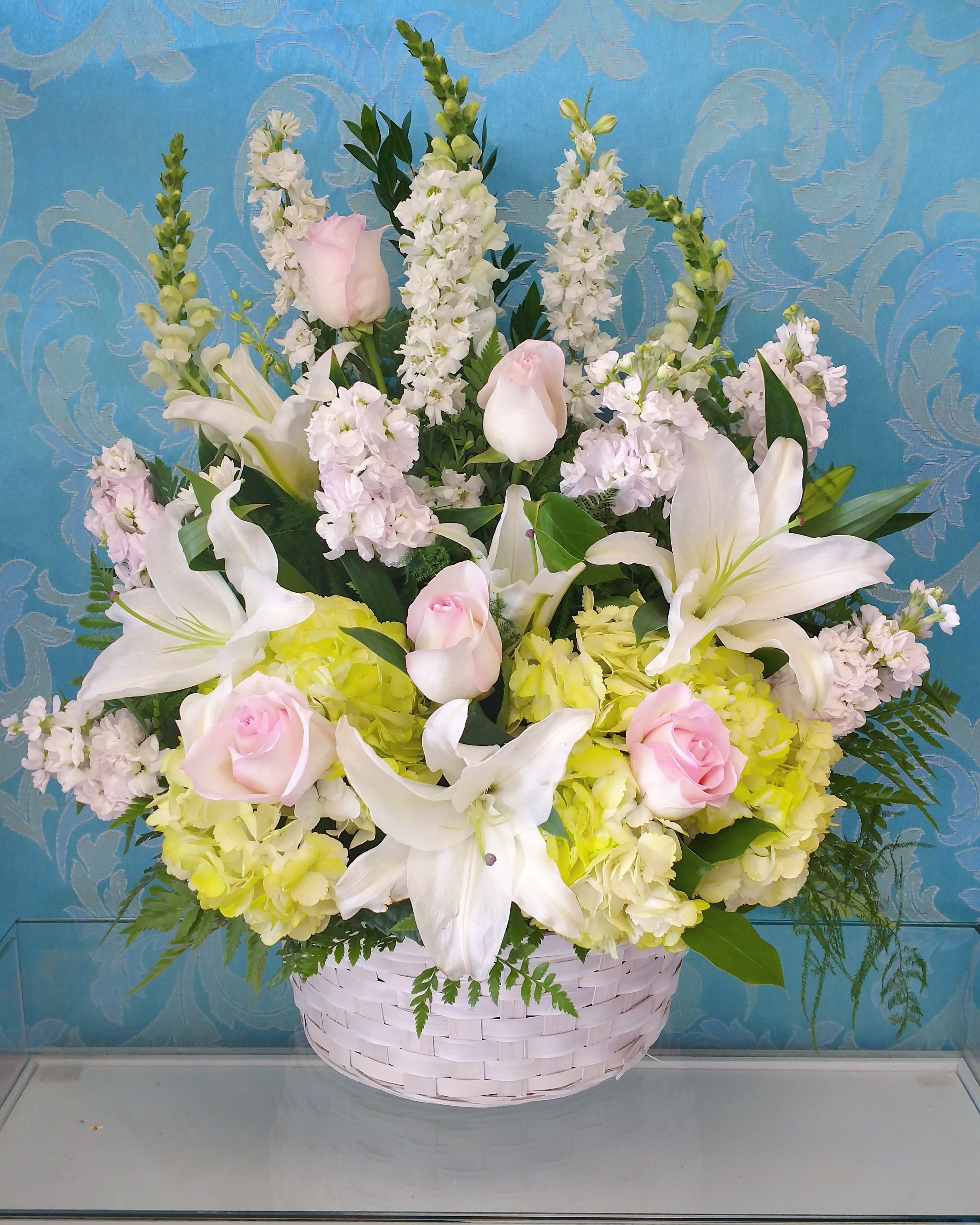 Basket arrangement of white lilies, pink roses, and pale hydrangeas