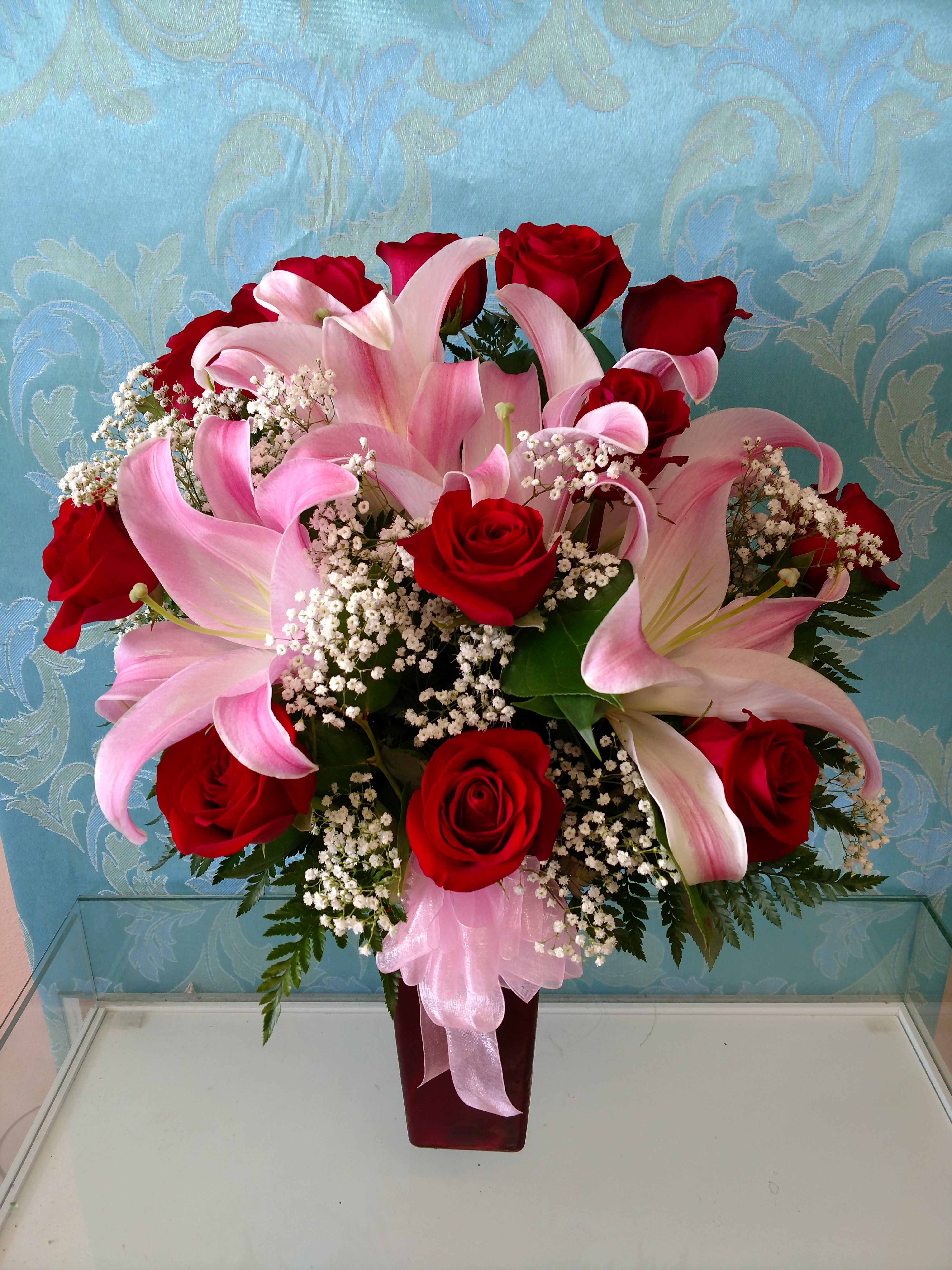 Red roses and pink lilies arranged in a tall vase with baby's breath