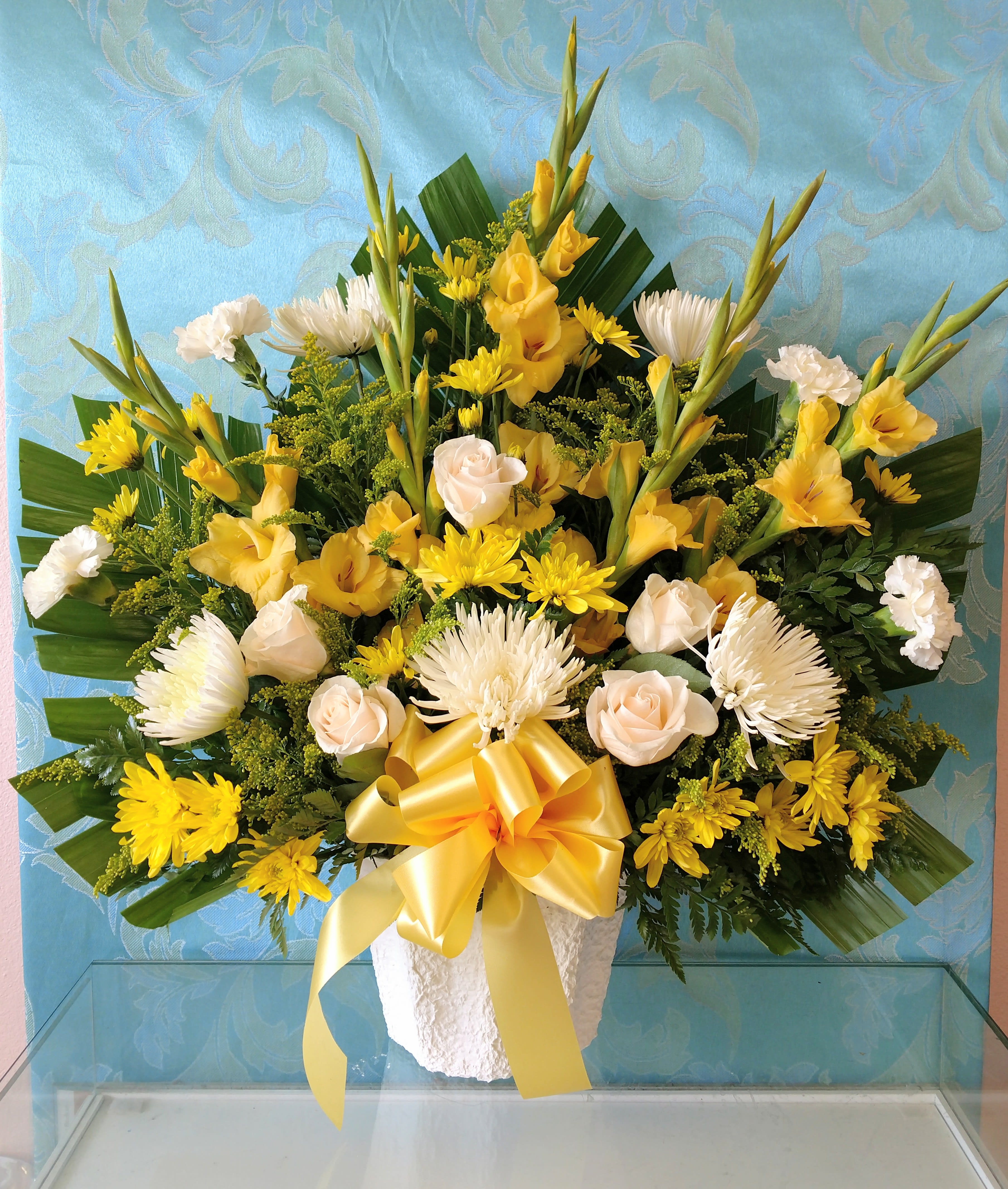 Yellow and white floral arrangement in a white vase with a yellow ribbon