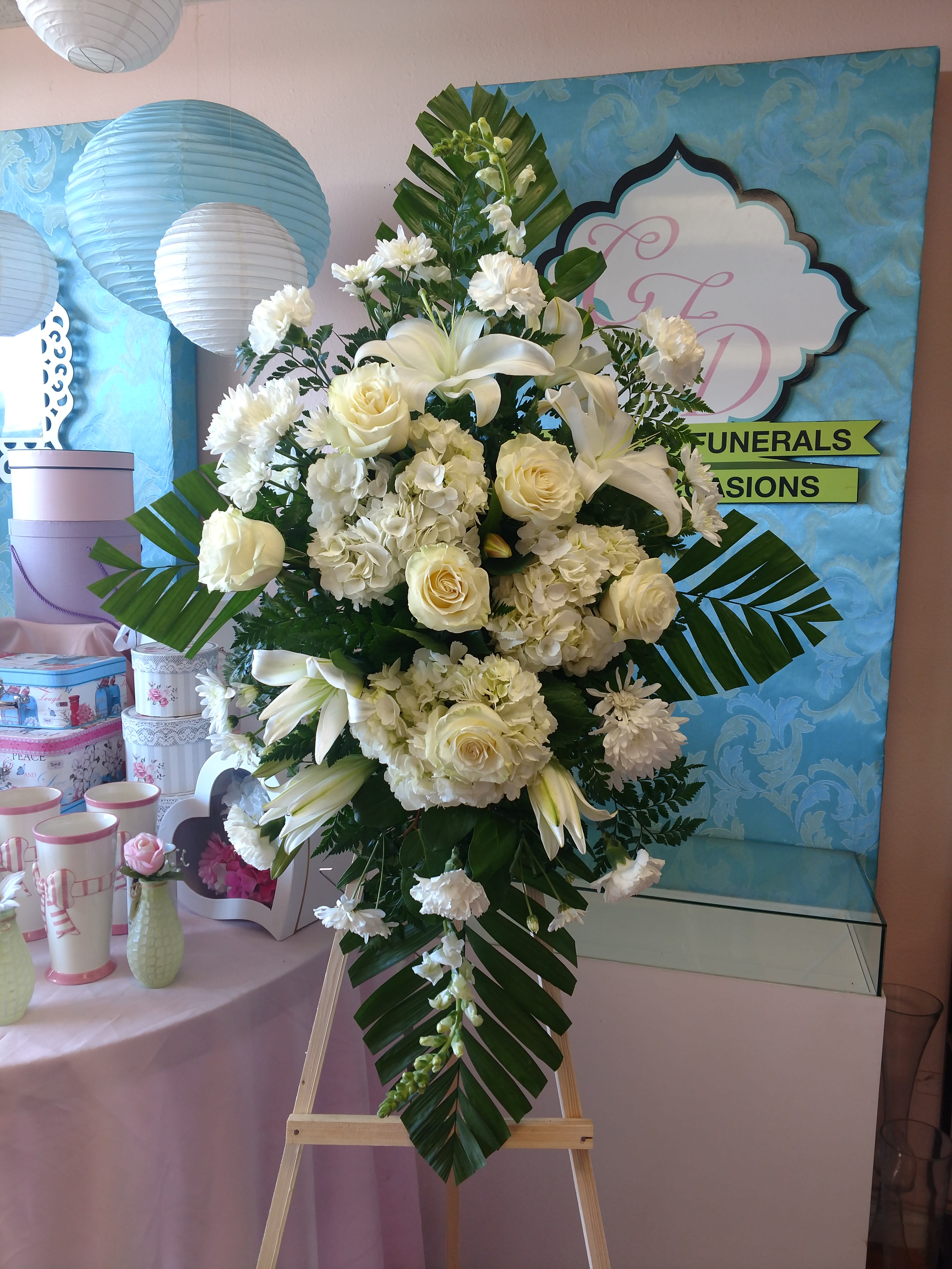 White floral standing spray on an easel with lilies and roses
