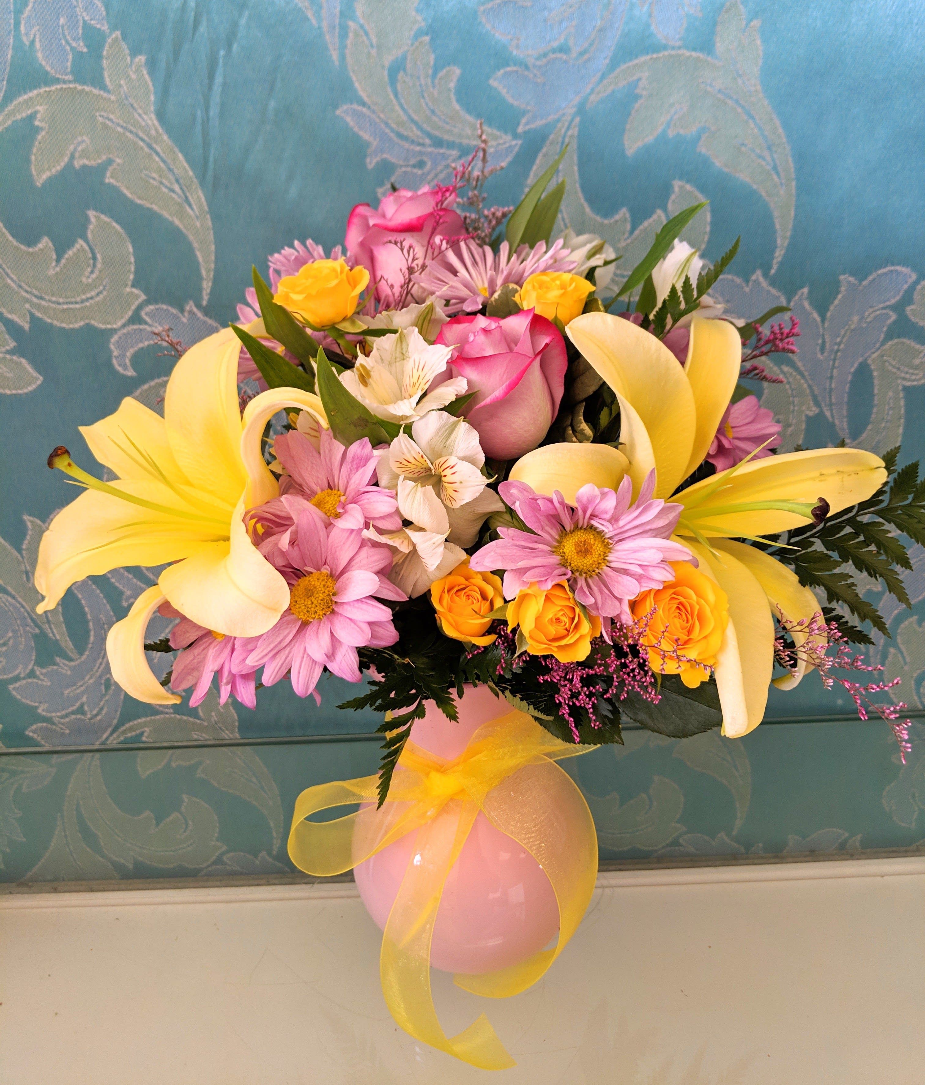 Pink and yellow flower arrangement in a pink vase with a yellow ribbon