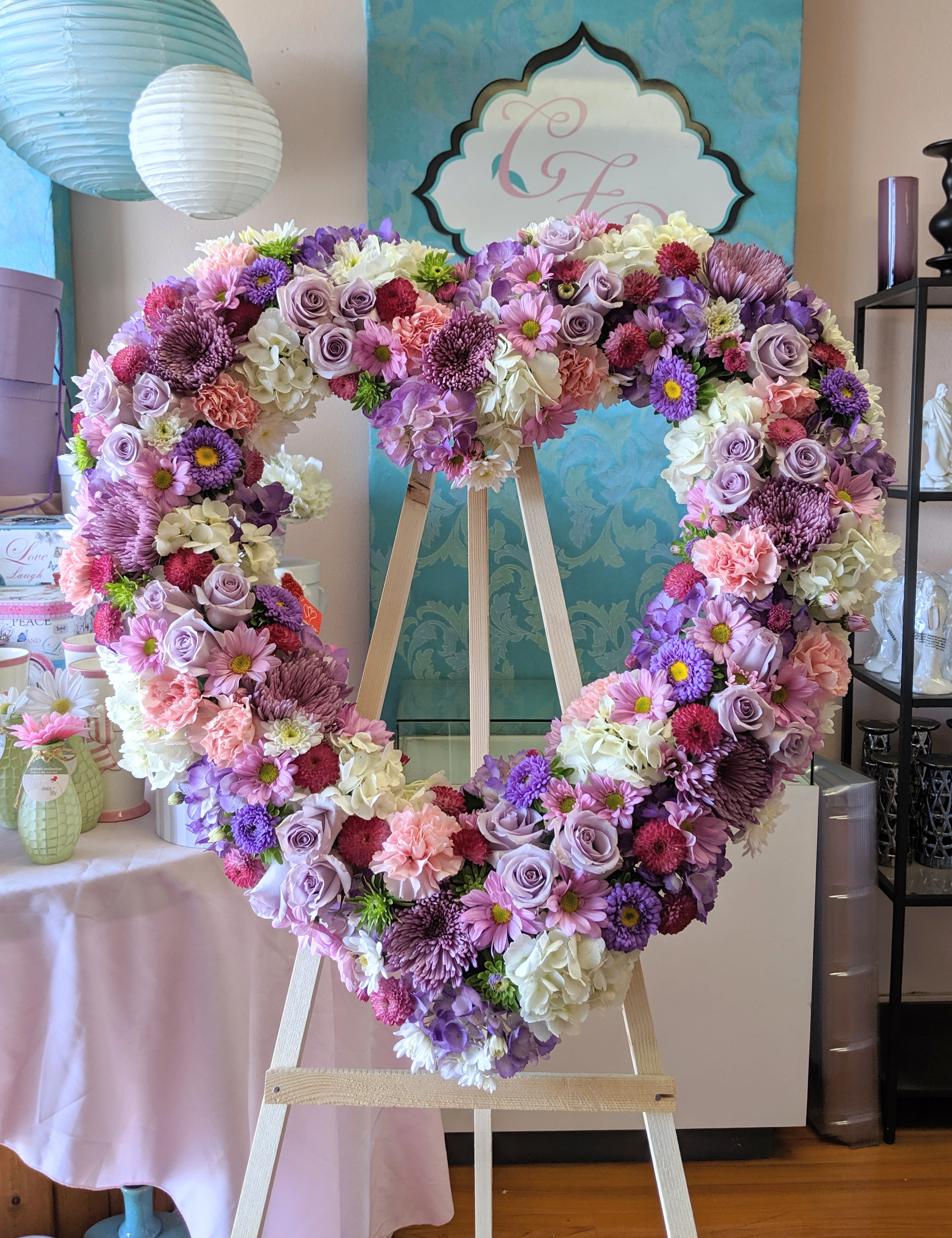 Large heart-shaped floral wreath on a wooden easel in pink, purple, and white.